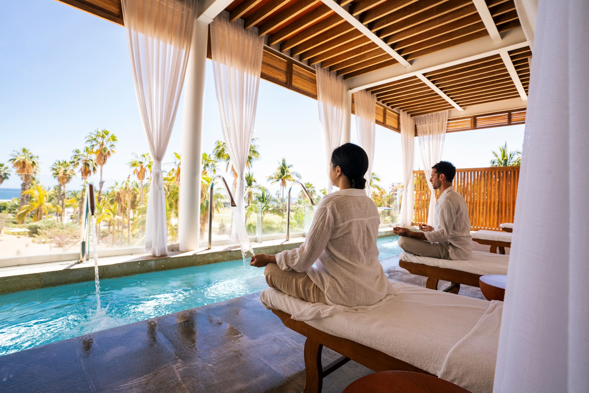 a man and woman sitting on massage tables by a pool