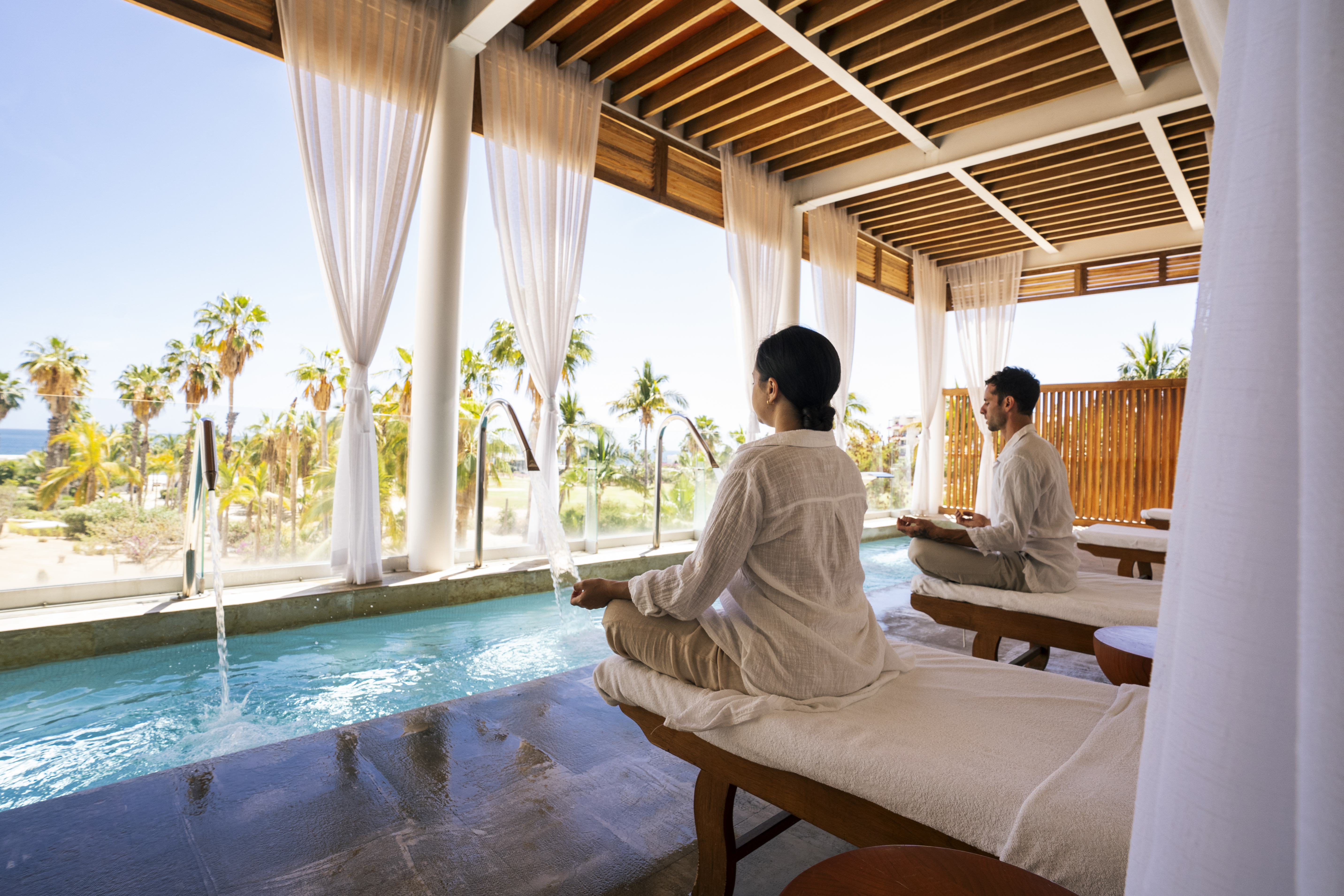 a man and woman sitting on massage tables by a pool