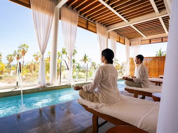 a man and woman sitting on massage tables by a pool