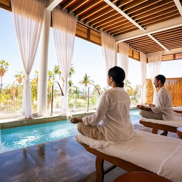 a man and woman sitting on massage tables by a pool