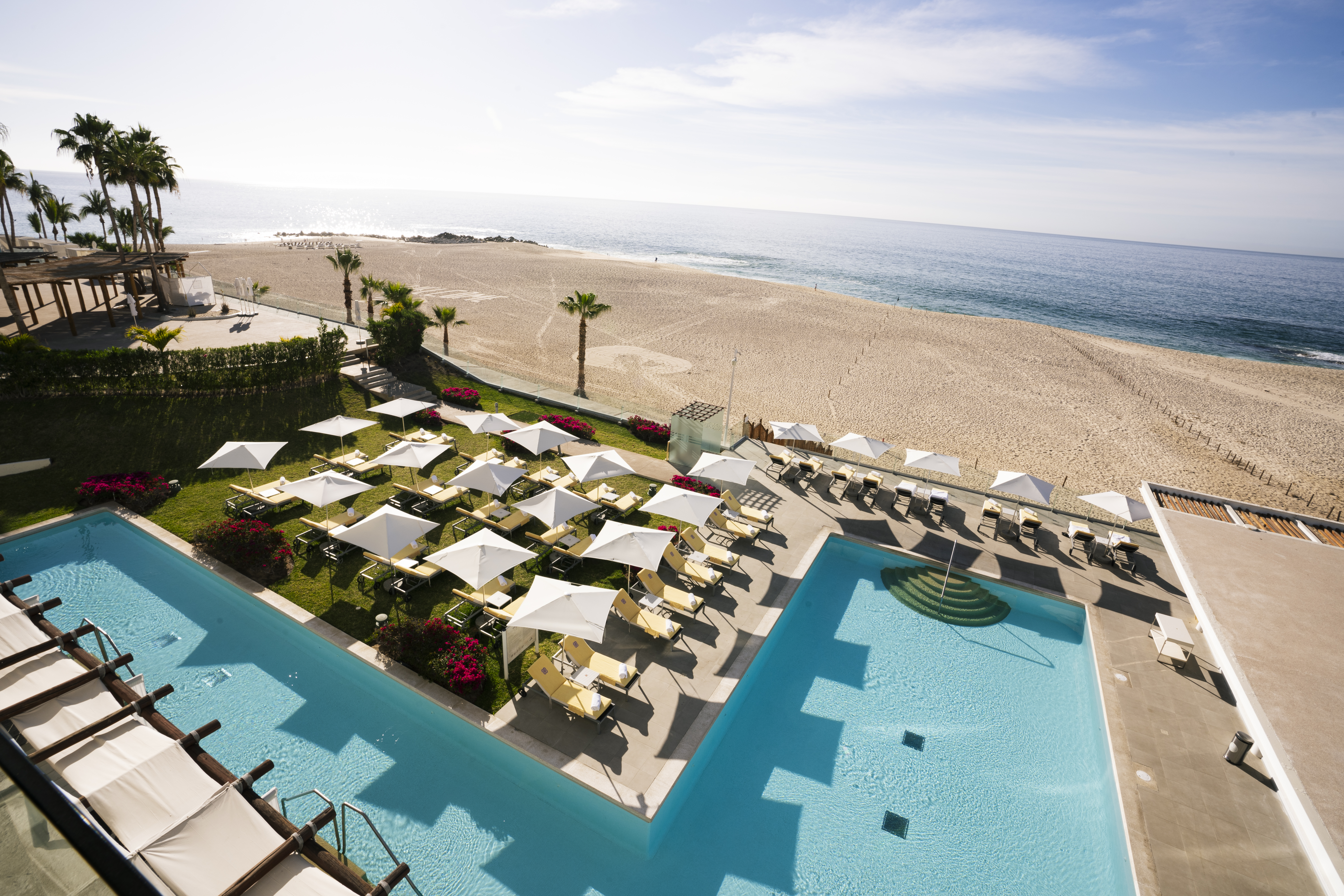 Oceanfront resort pools, beach, lounge chairs, umbrellas, palm trees.