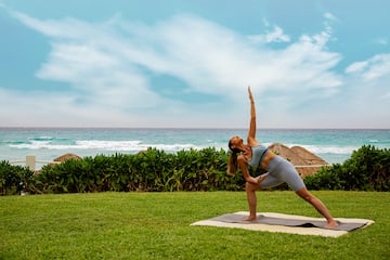a woman doing yoga on a mat in the grass by the ocean