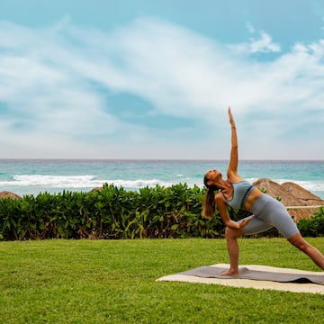 a woman doing yoga on a mat in the grass by the ocean