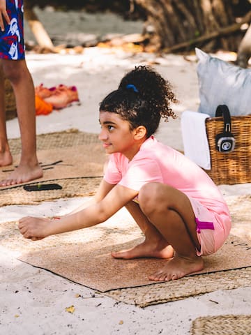 a girl kneeling on mat on the sand