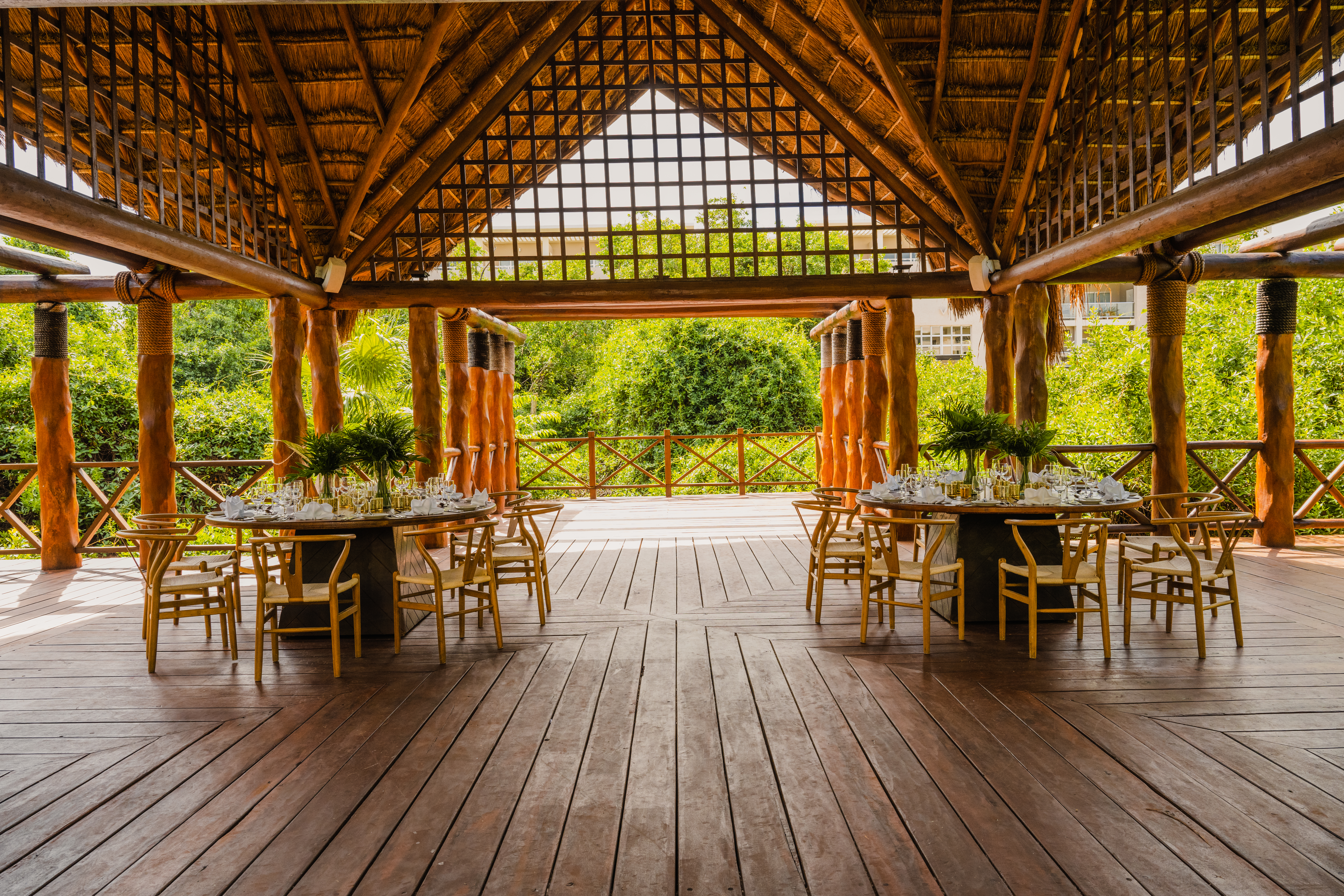 Thatch-roof outdoor restaurant with set tables and lush tropical views.