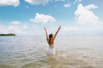 a woman in a white dress standing in water with her arms raised