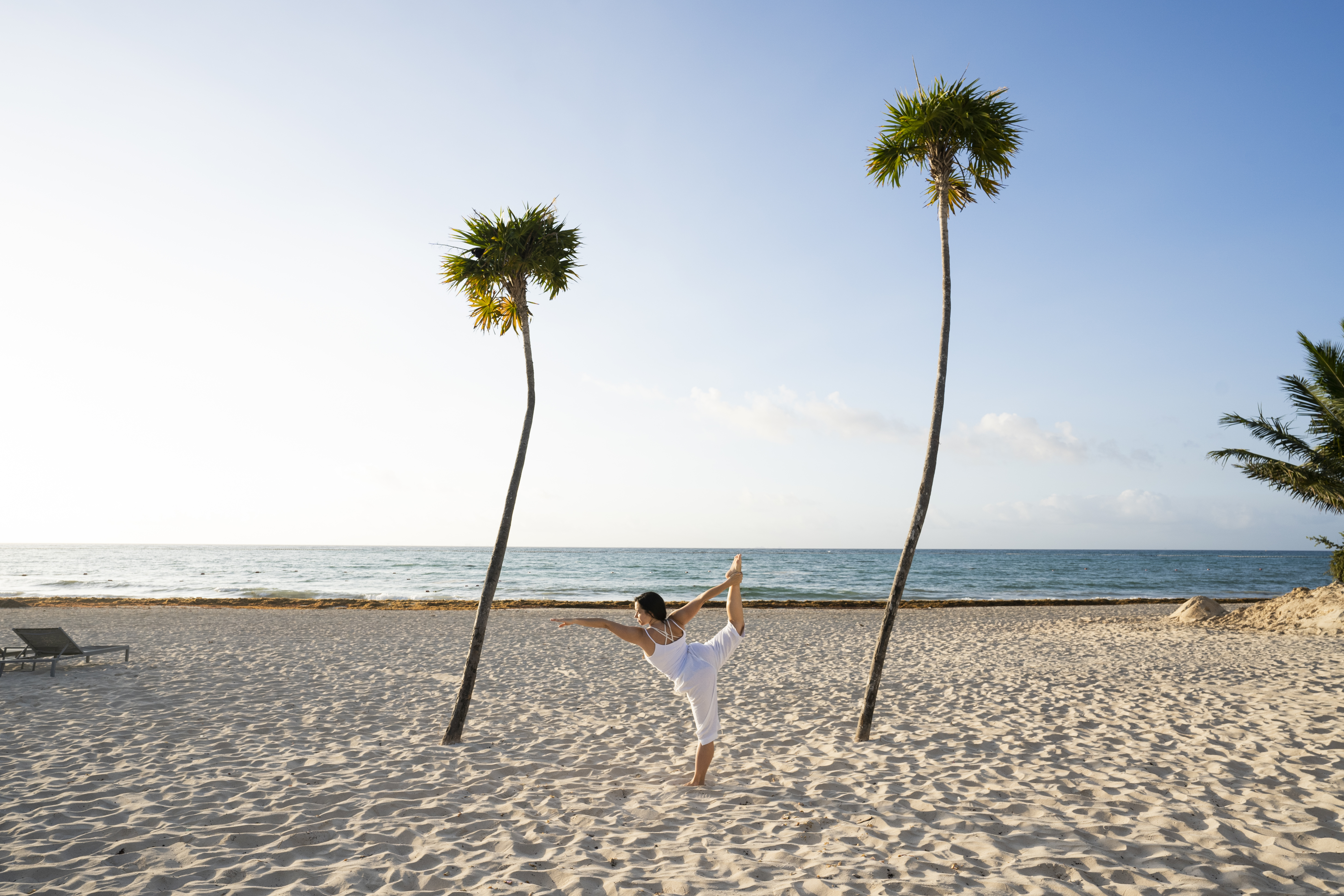 a woman standing on one leg on a beach with palm trees