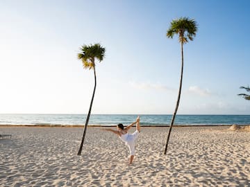 a woman standing on one leg on a beach with palm trees