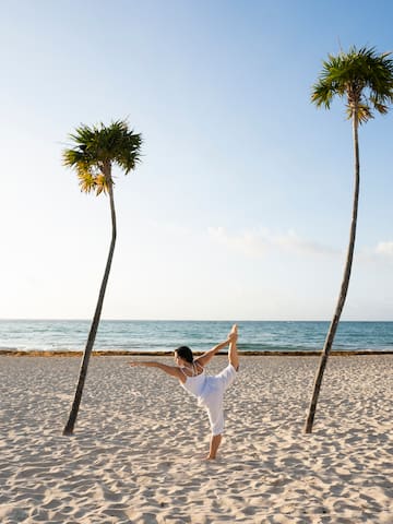 a woman standing on one leg on a beach with palm trees