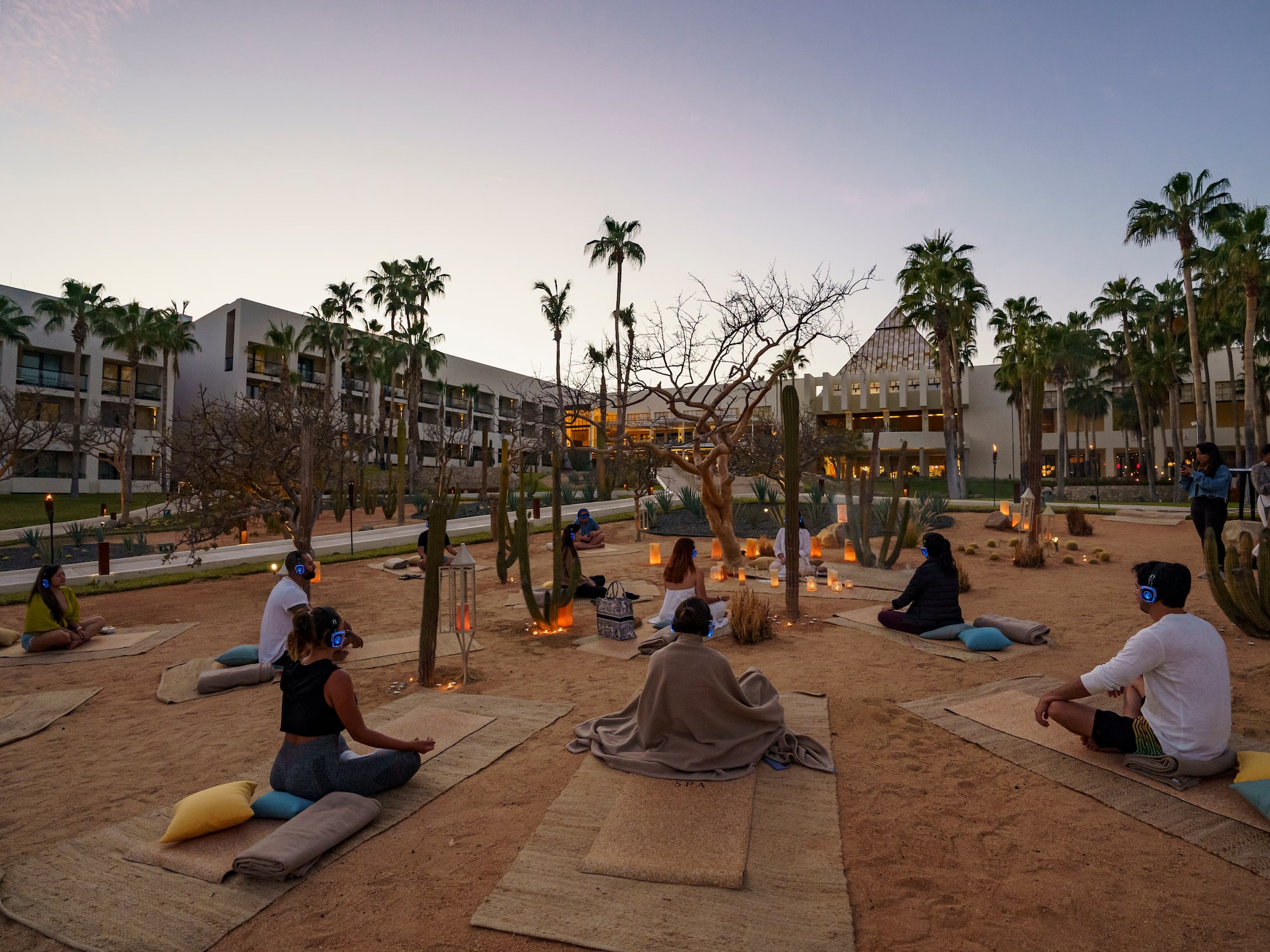 a group of people sitting on mats in a courtyard with palm trees
