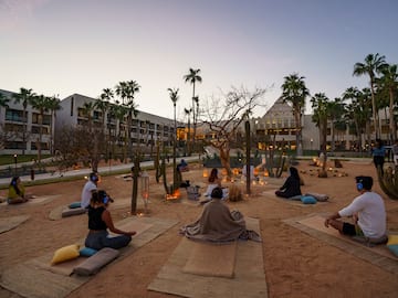 a group of people sitting on mats in a courtyard with palm trees