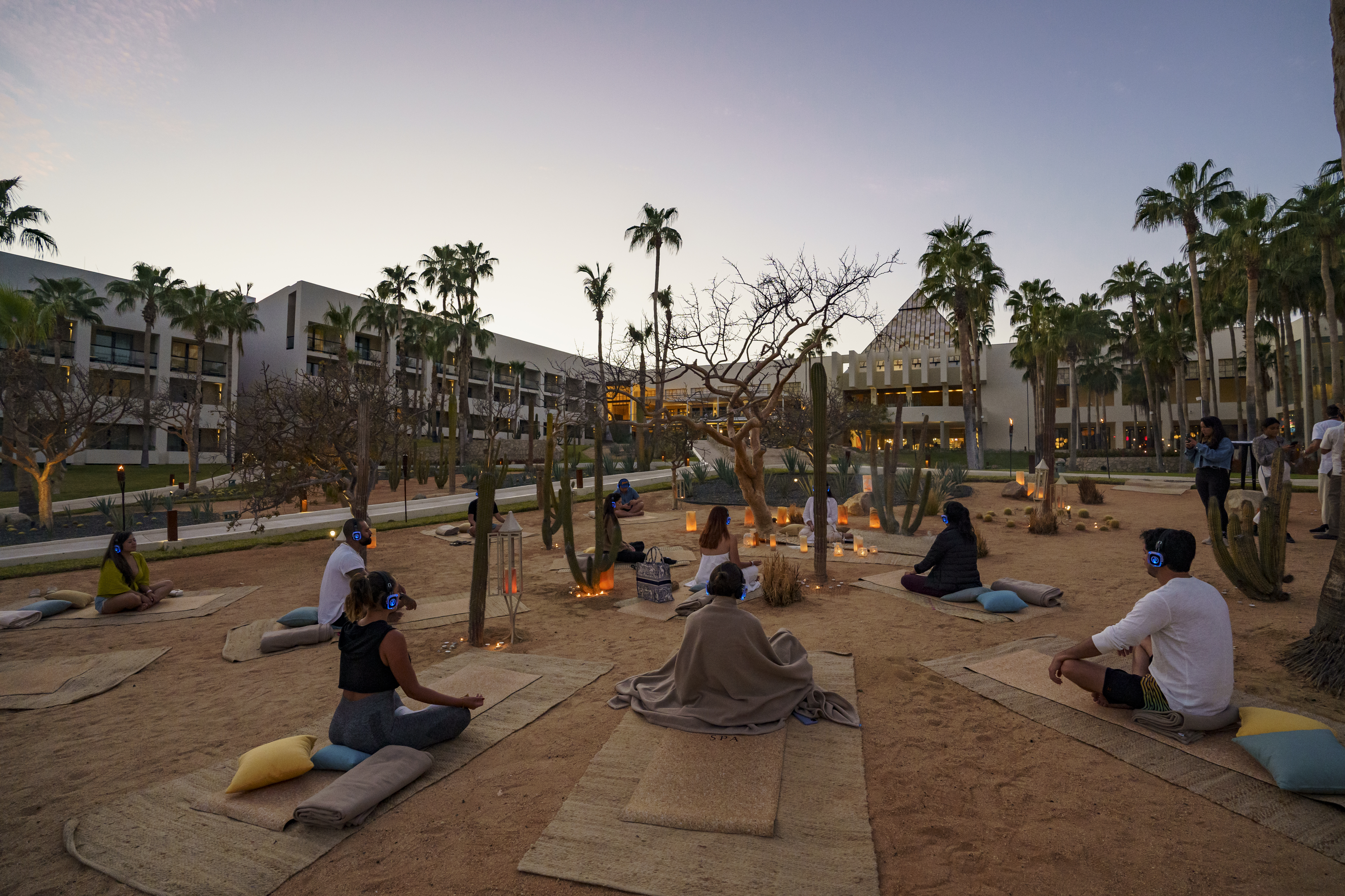 a group of people sitting on mats in a courtyard with palm trees