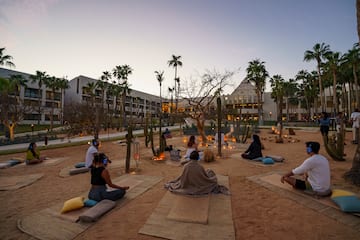 a group of people sitting on mats in a courtyard with palm trees