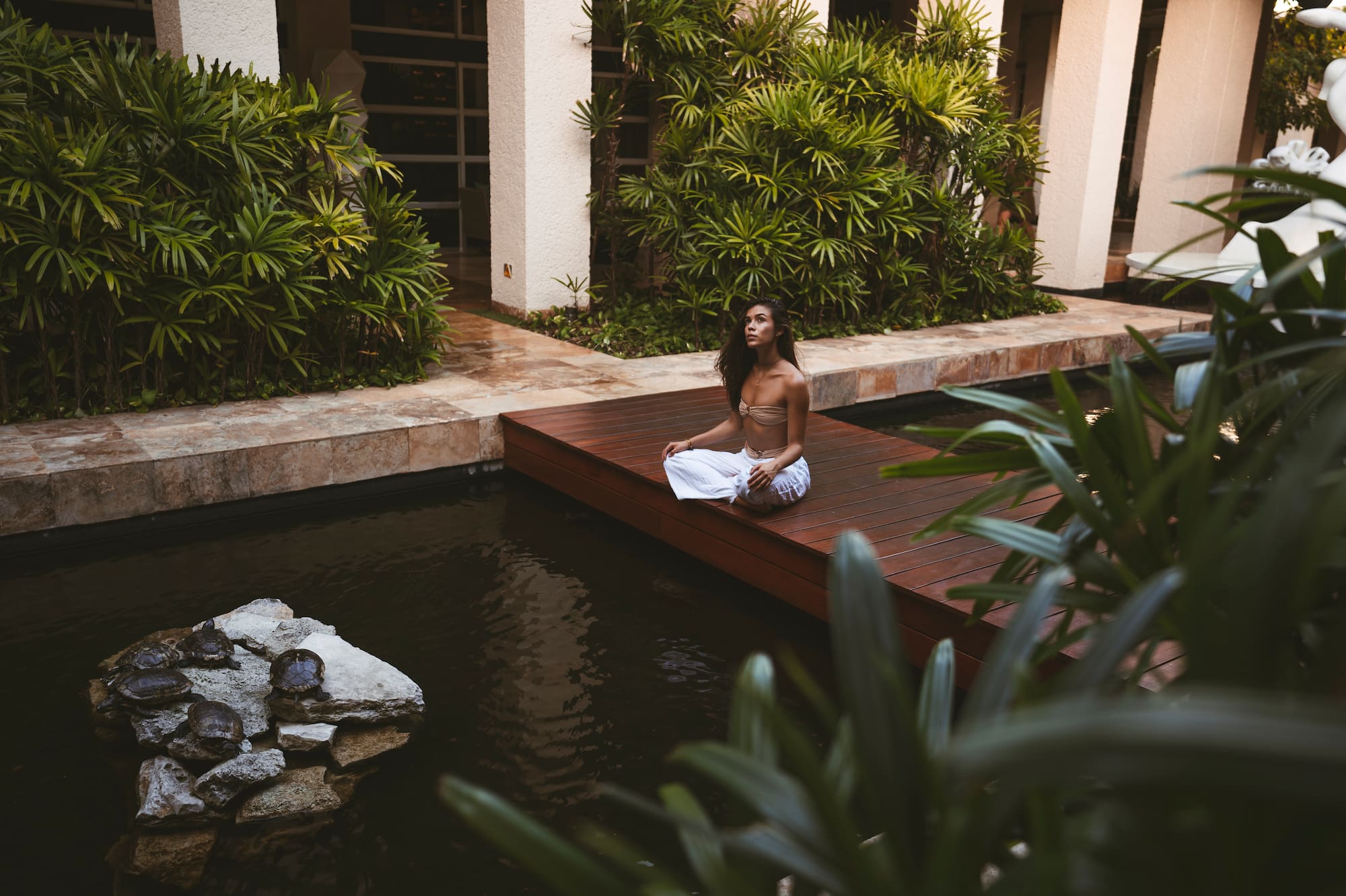 a woman sitting on a wood platform in front of a pond