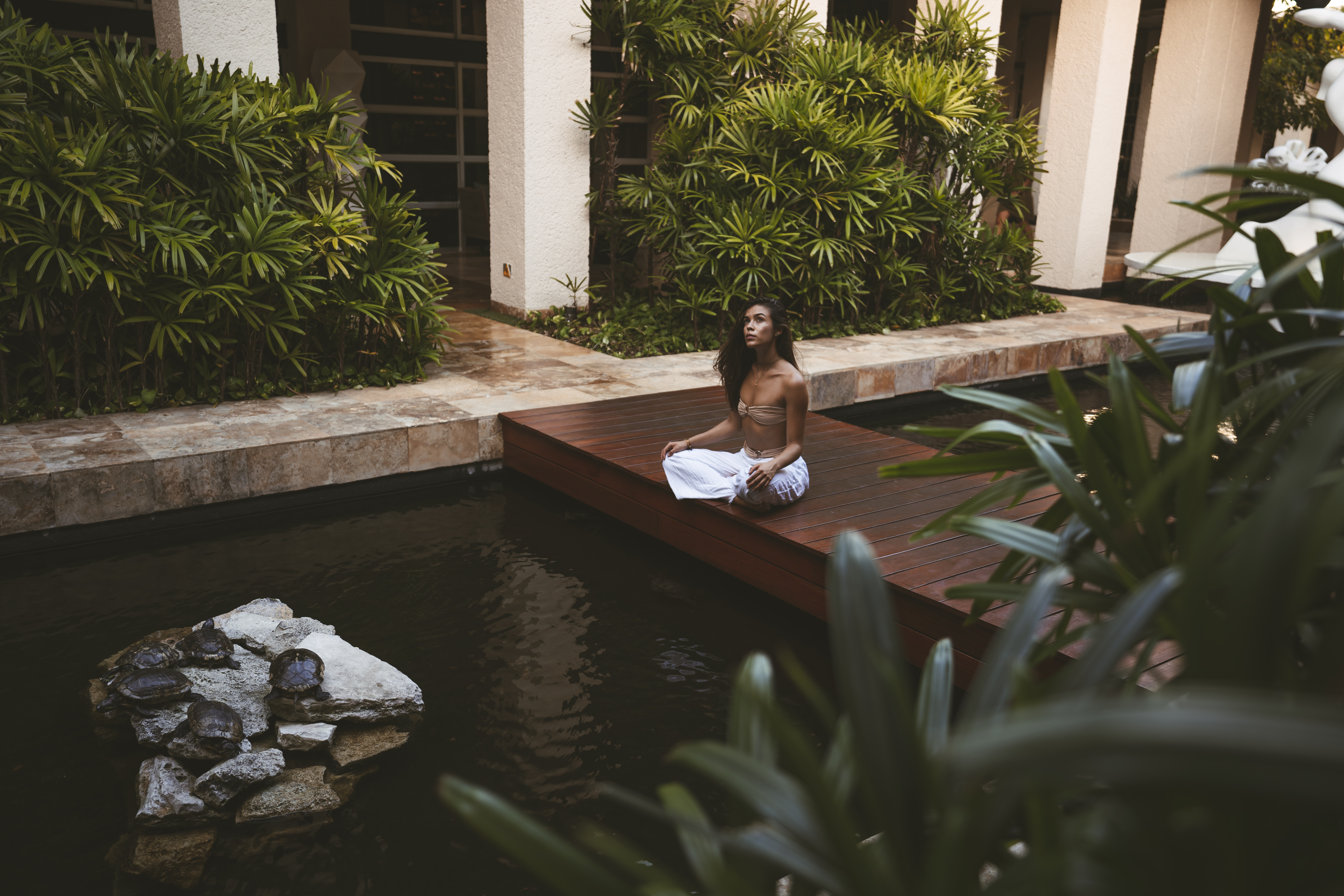 a woman sitting on a wood platform in front of a pond