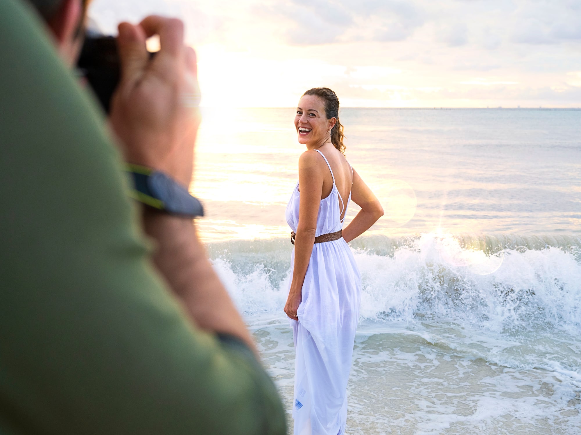 a man taking a picture of a woman in a white dress on a beach