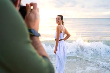 a man taking a picture of a woman in a white dress on a beach