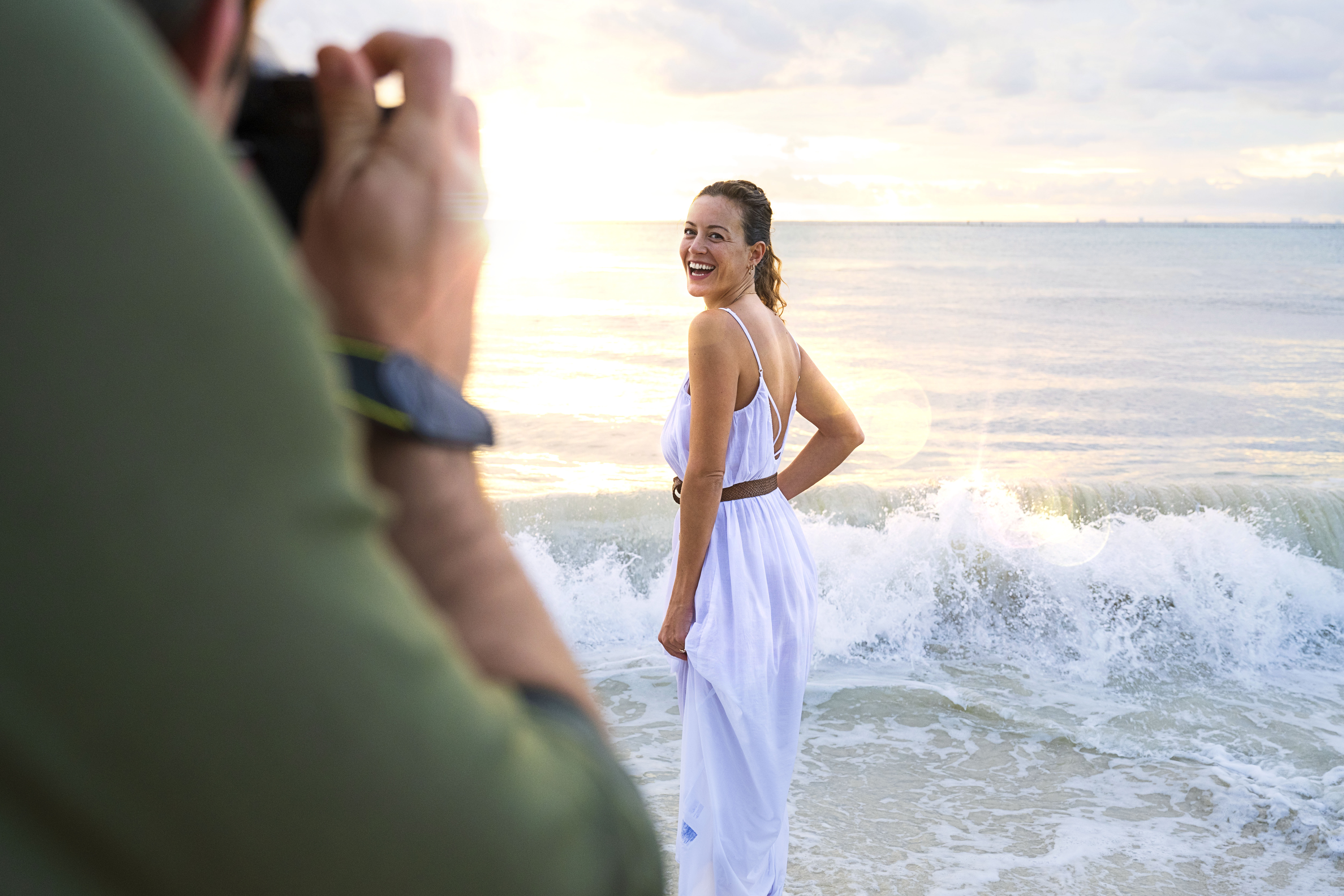 a man taking a picture of a woman in a white dress on a beach