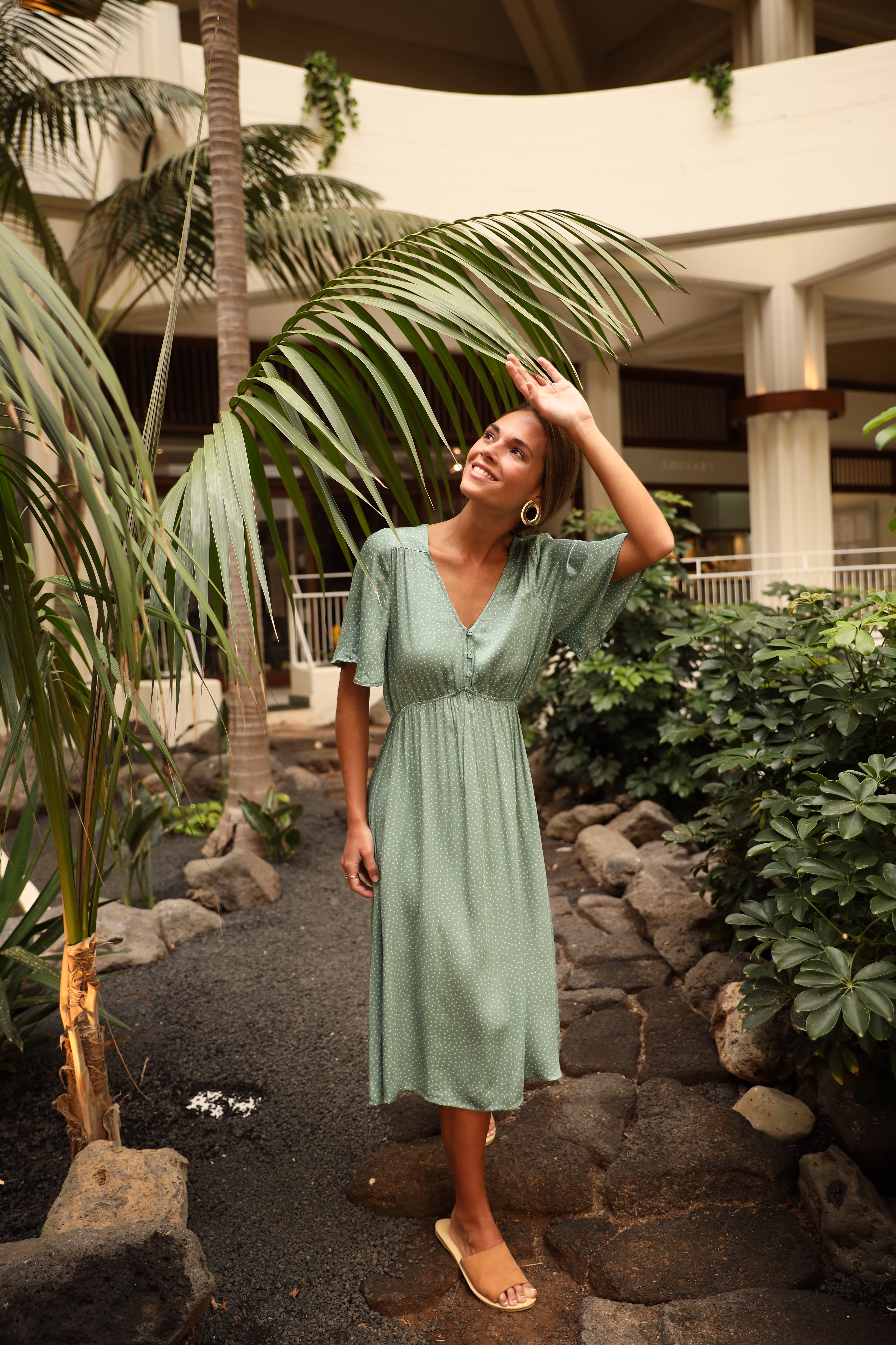 a woman in a dress standing next to a palm tree