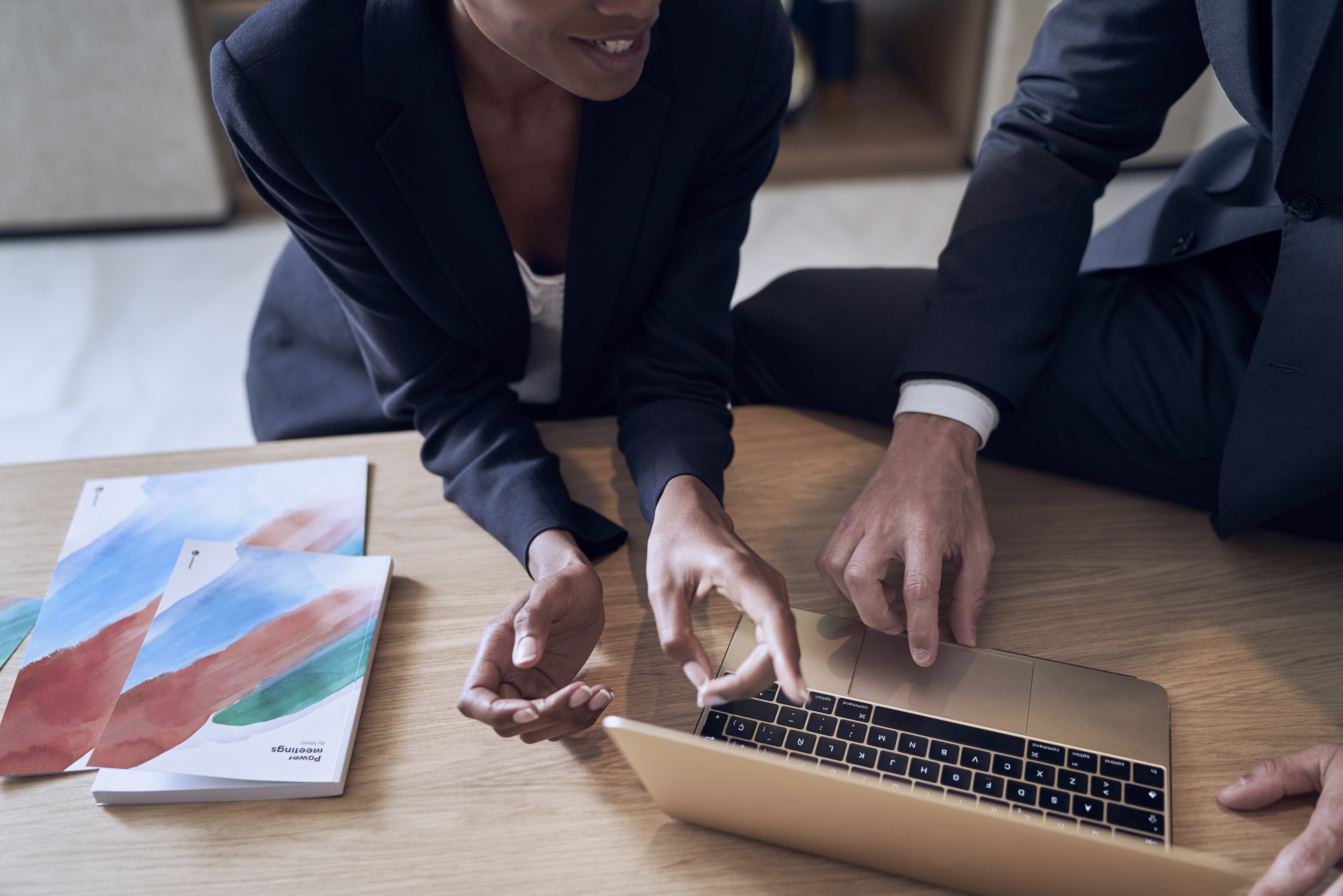 Two professionals collaborating on a gold laptop during a business meeting.