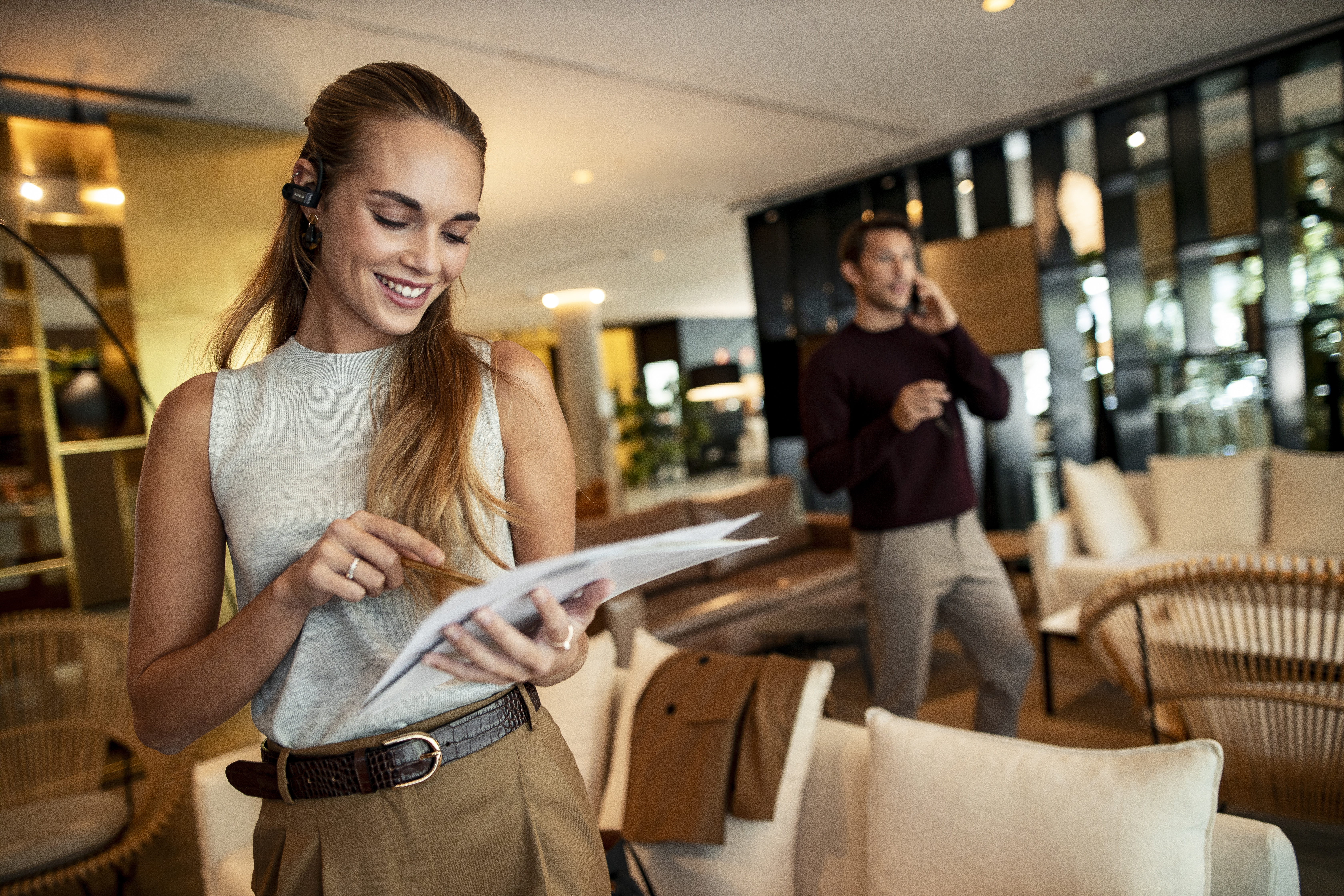 a woman holding papers and smiling while a man talking on the phone