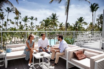 a group of people sitting on a deck with a pool and palm trees