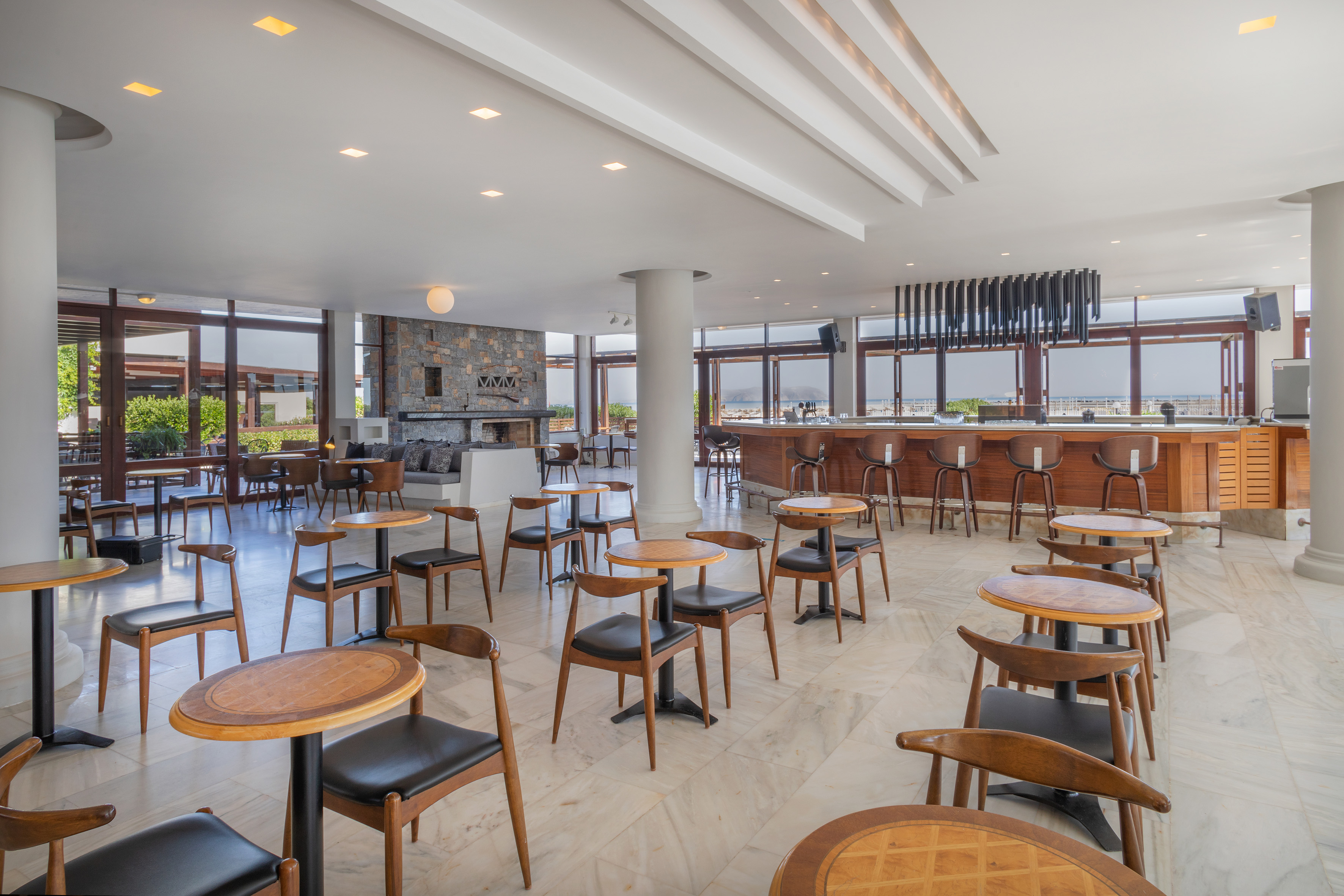 Modern hotel lounge bar with wooden seating, stone fireplace, bright interior.