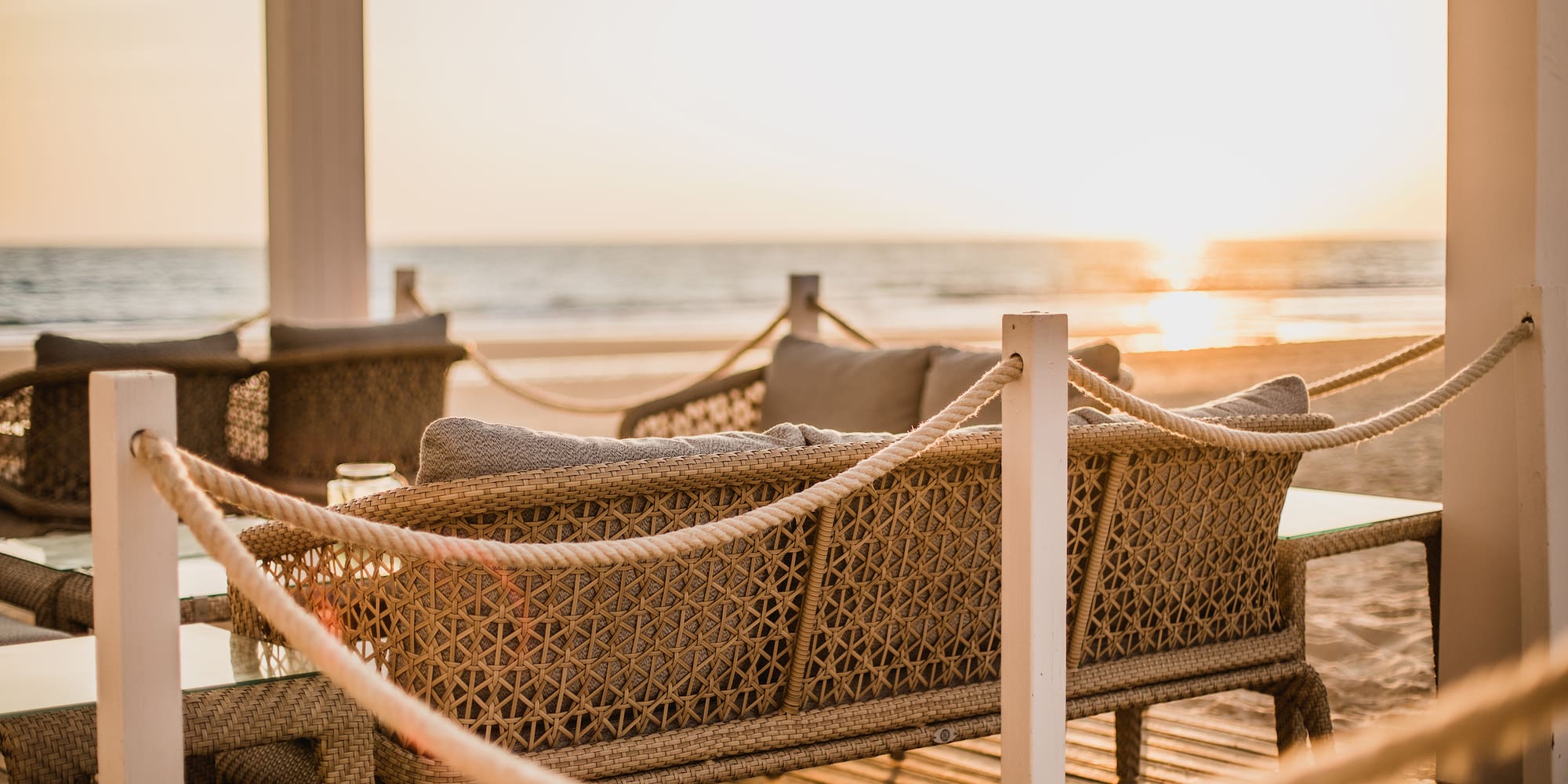 a wicker furniture on a deck with a beach in the background