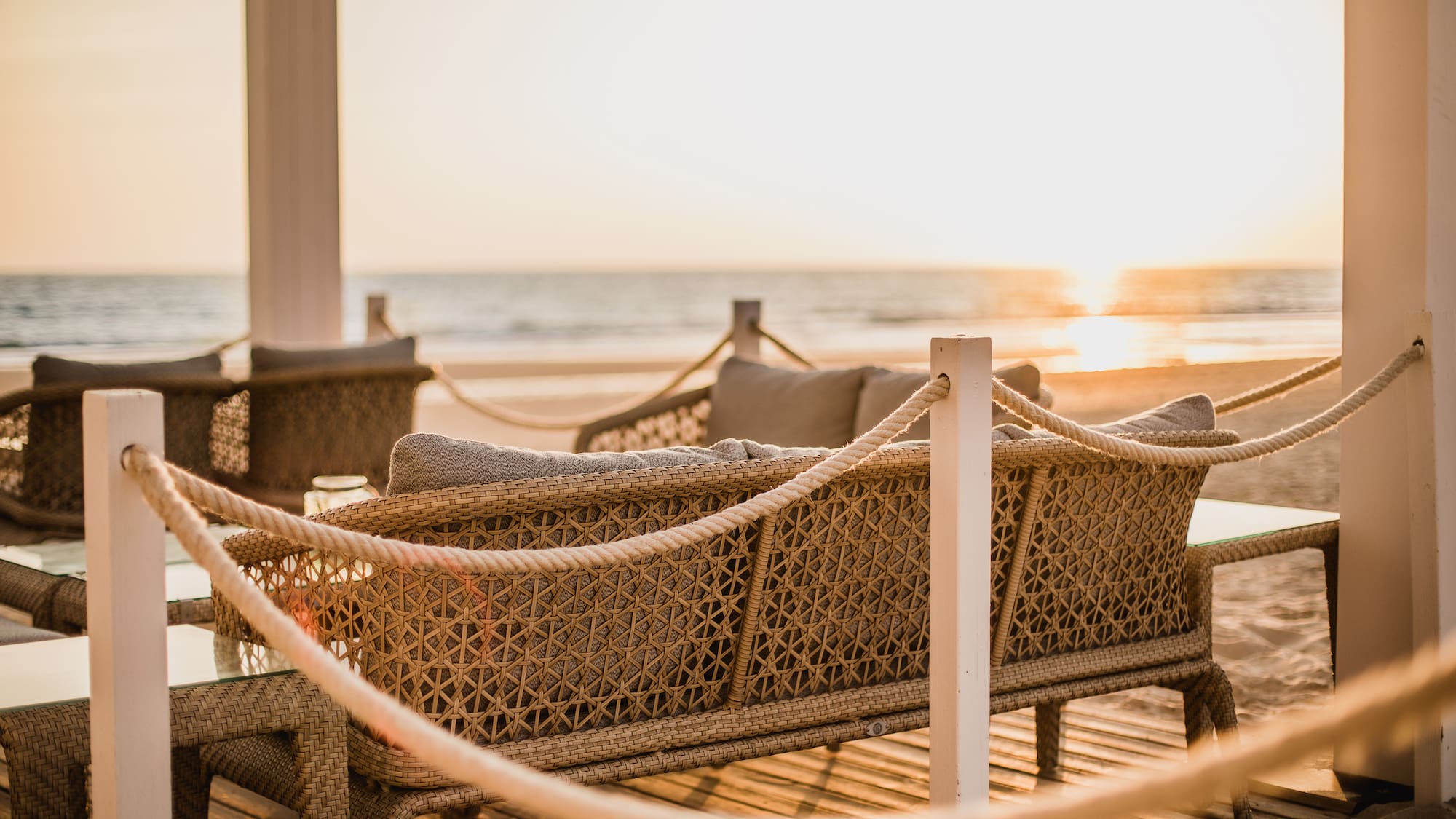 a wicker furniture on a deck with a beach in the background