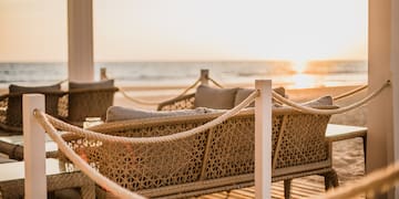 a wicker furniture on a deck with a beach in the background