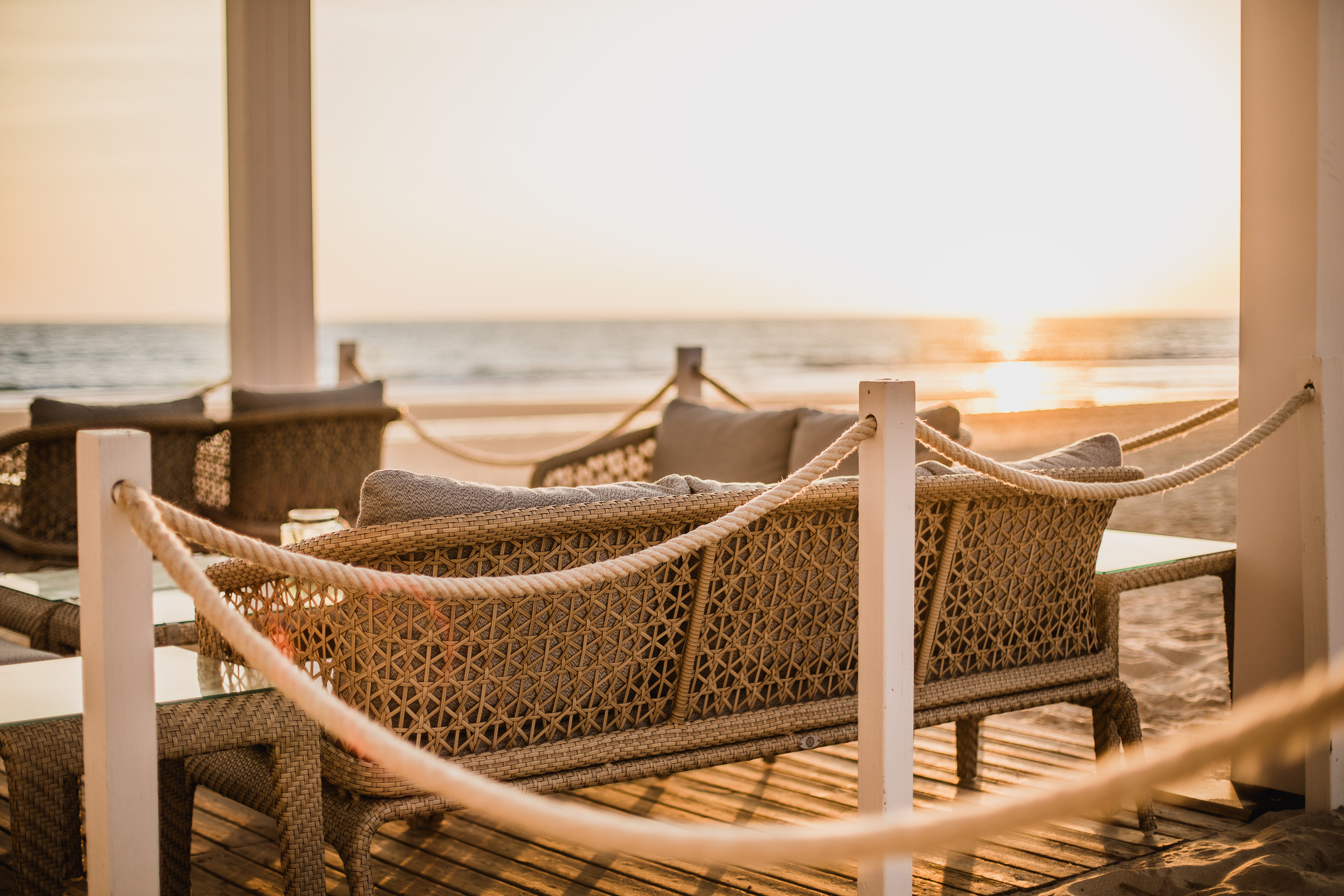 Luxury beach resort patio with wicker furniture and ocean sunset view.