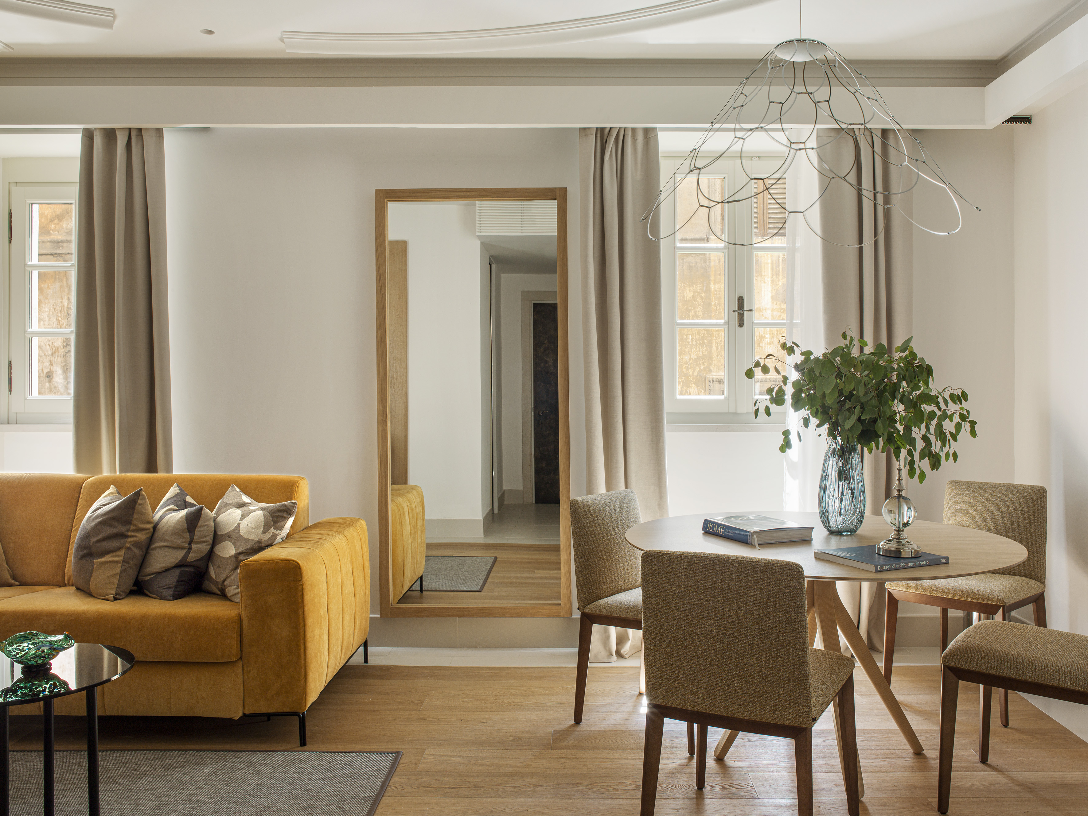 Modern living-dining room with gold sofa, wood table, and full-length mirror.