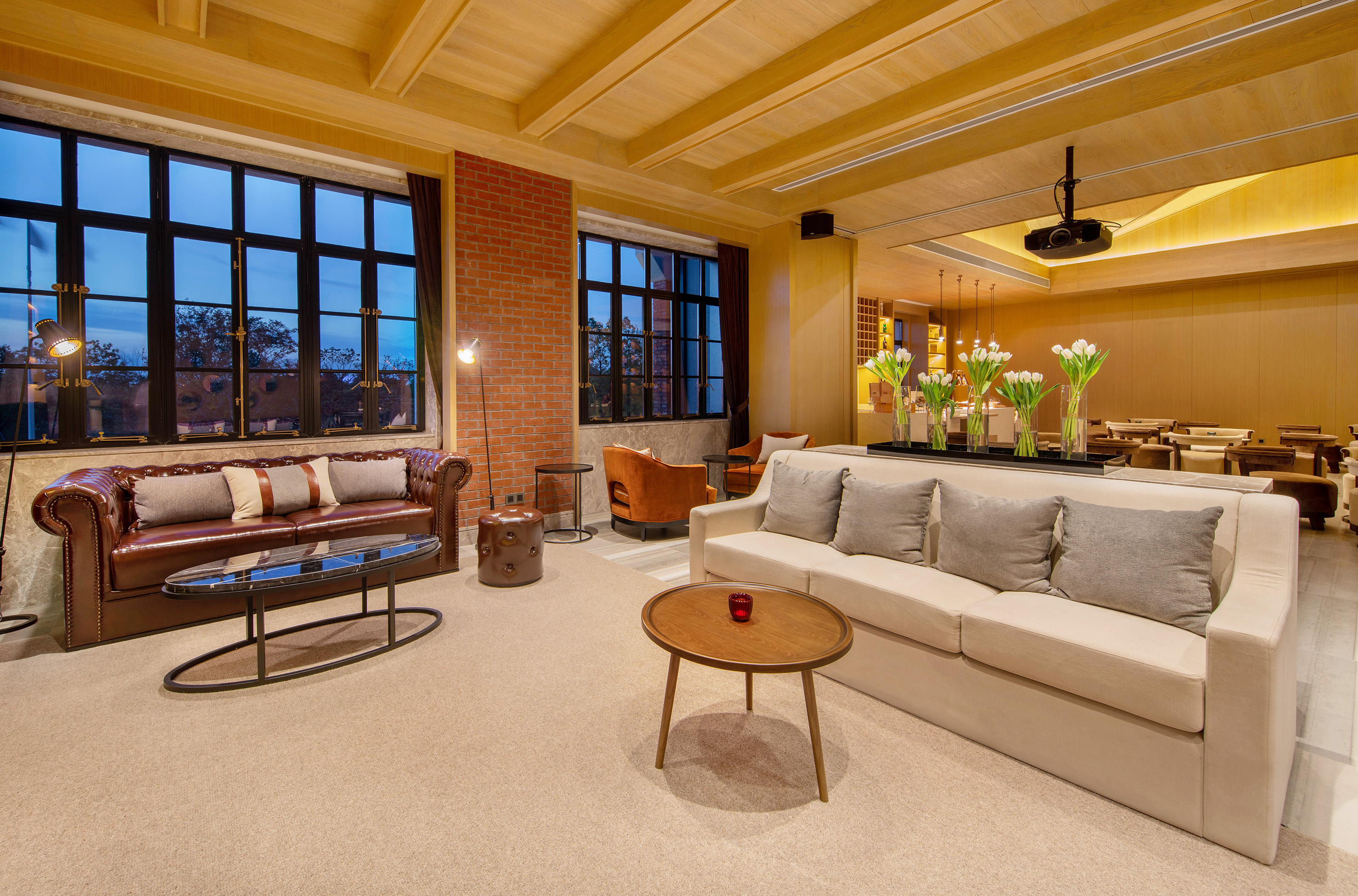 Lounge with leather and fabric sofas, large grid windows, brick wall, wood ceiling.