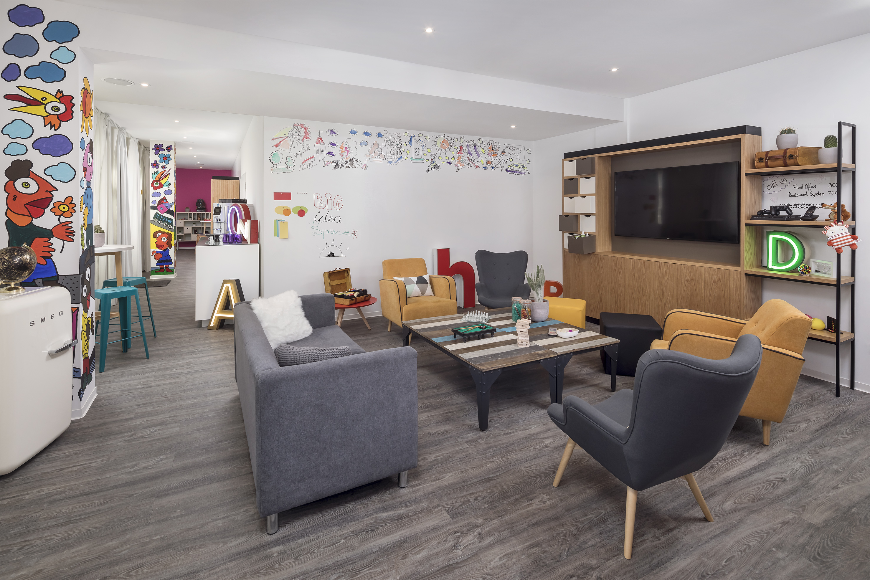 Colorful modern lounge with creative wall art, sofa, armchairs, TV, and games.