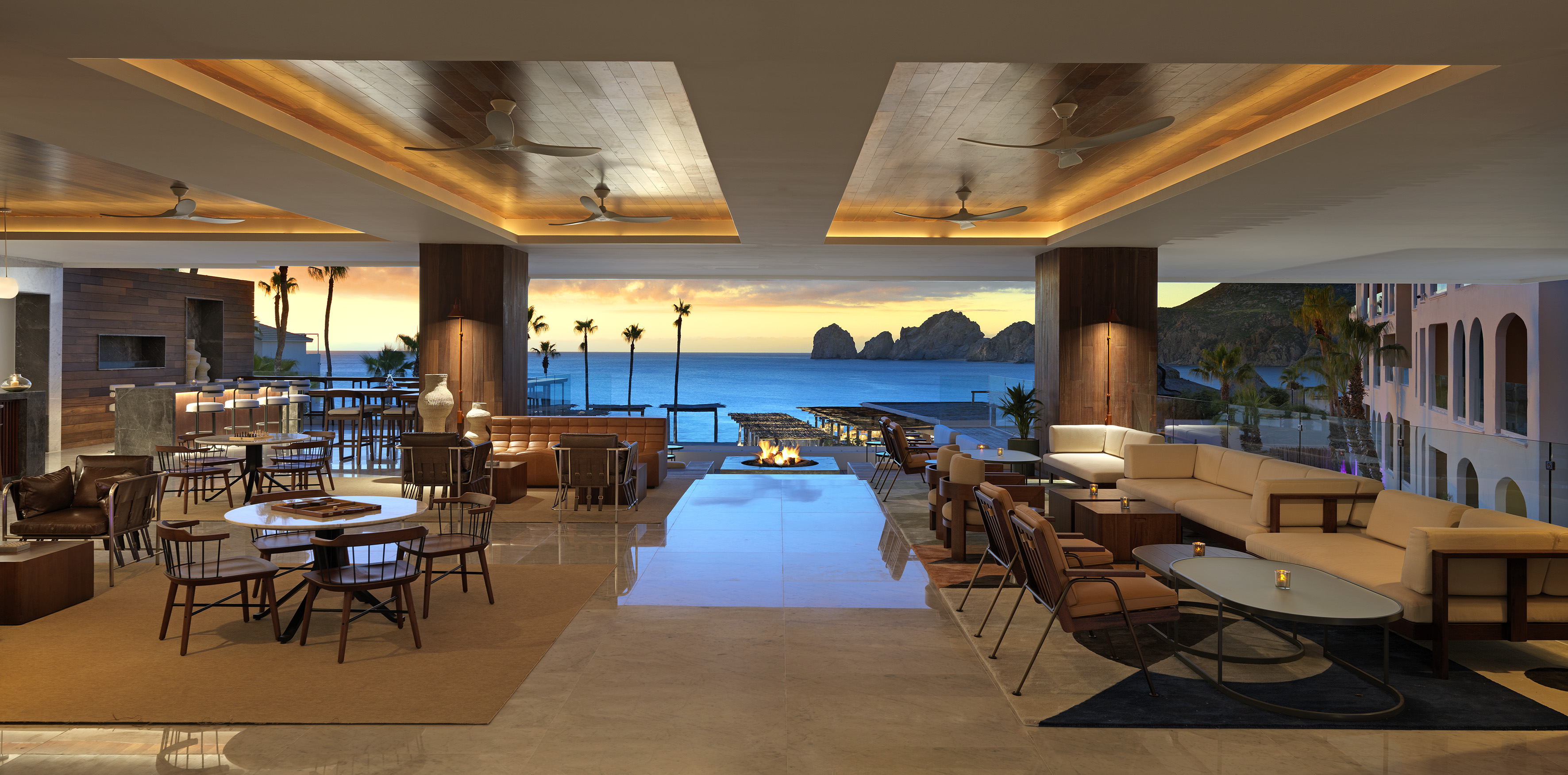 Modern resort lounge with ocean view at sunset, stylish seating, and fire pit.