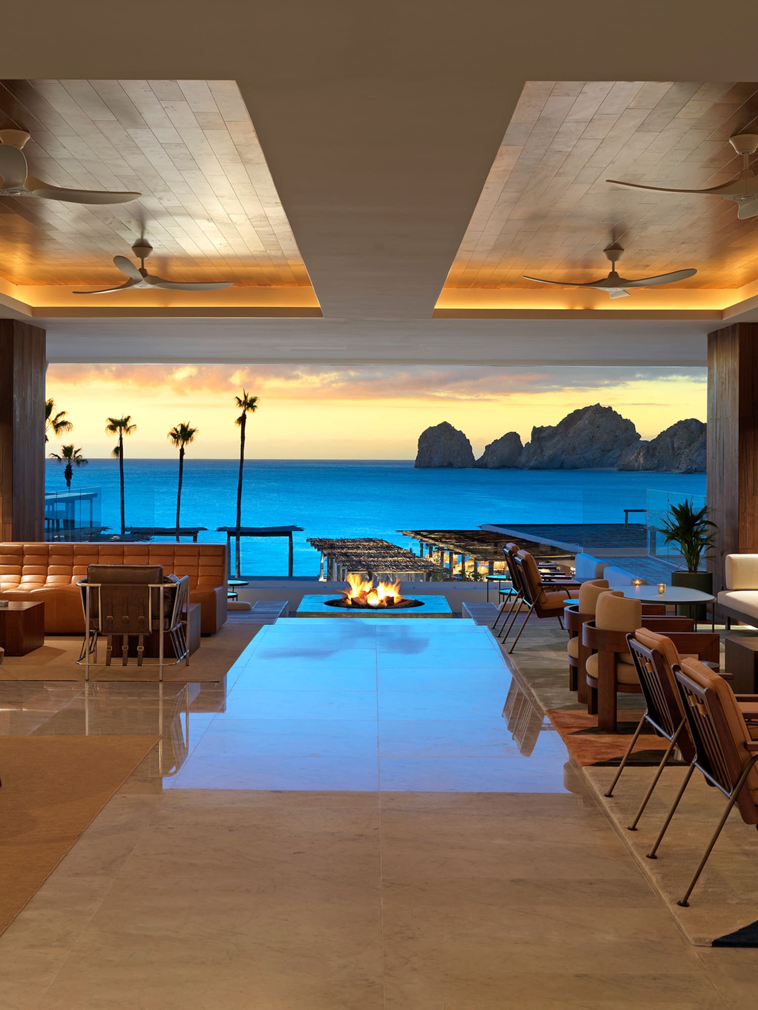 Modern resort lounge with ocean view at sunset, stylish seating, and fire pit.