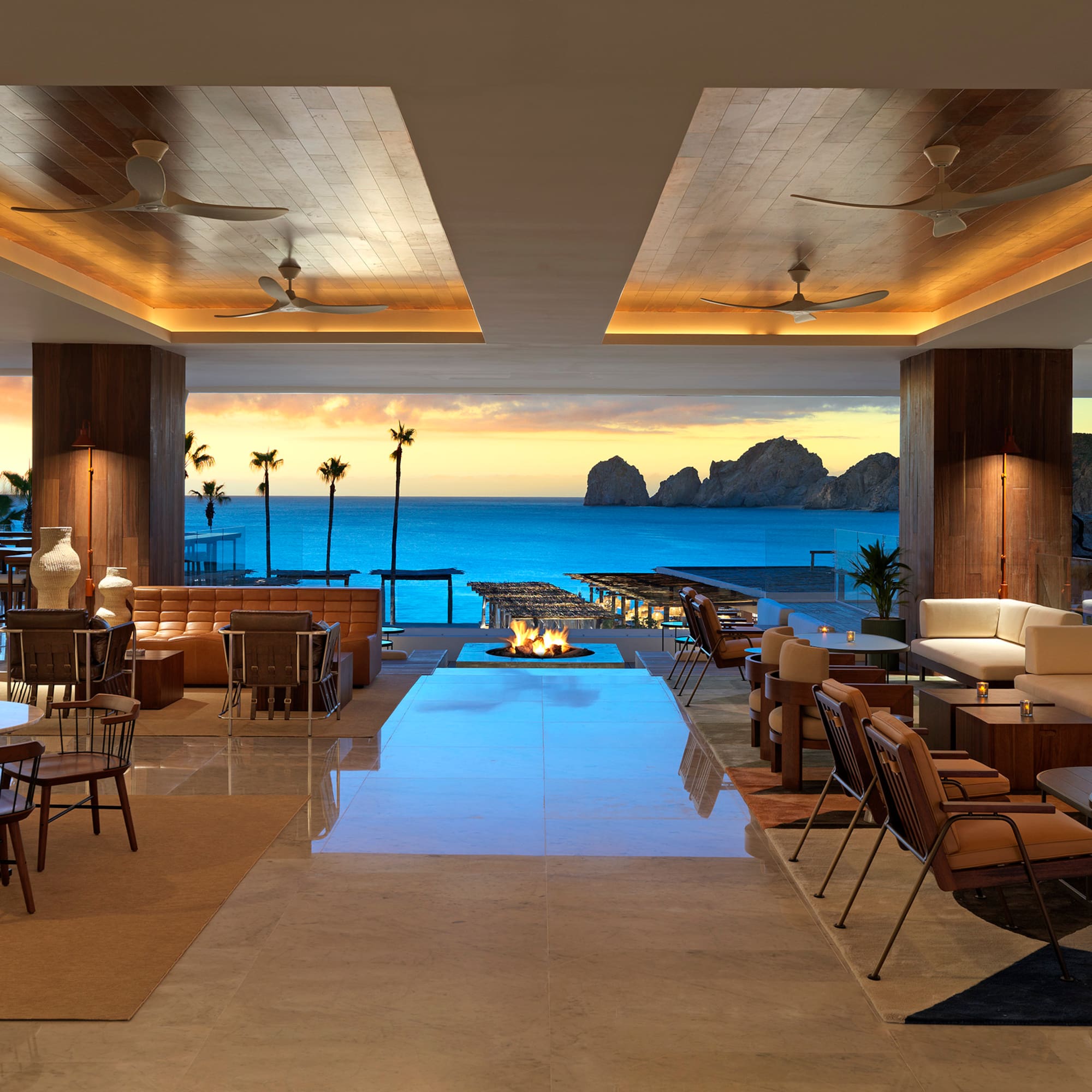 Modern hotel lounge overlooking ocean and El Arco at sunset with fire pit.