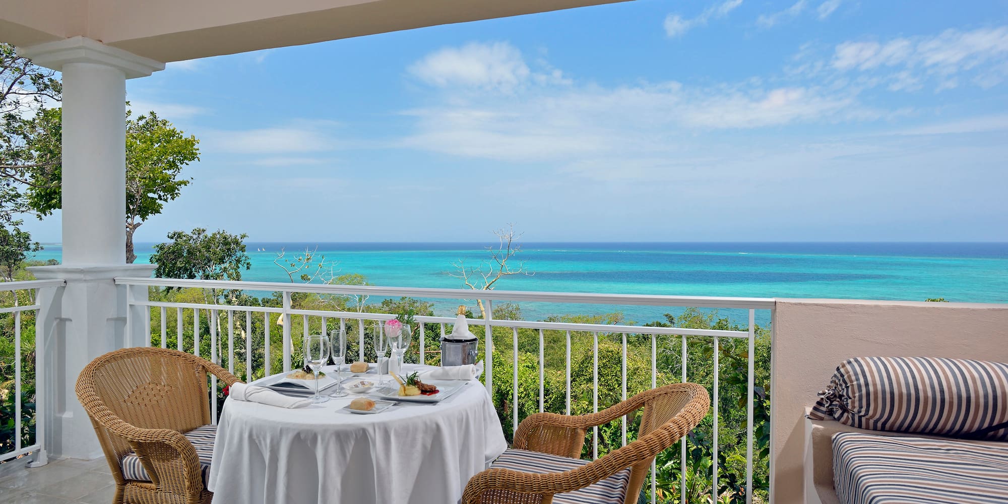 a table with a chair and a table set on a balcony overlooking the ocean