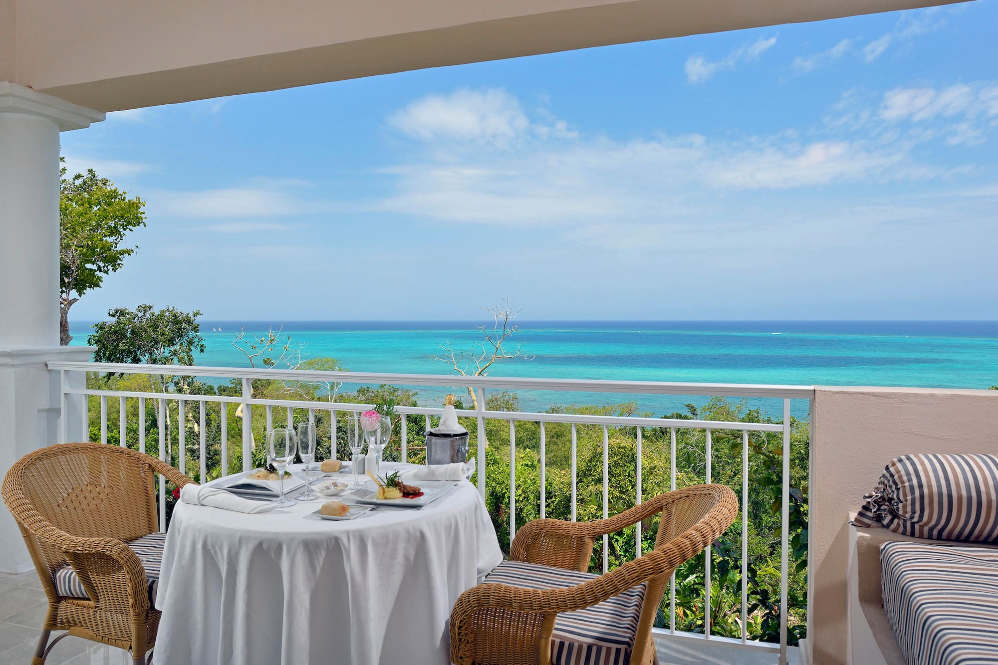 a table with a chair and a table set on a balcony overlooking the ocean