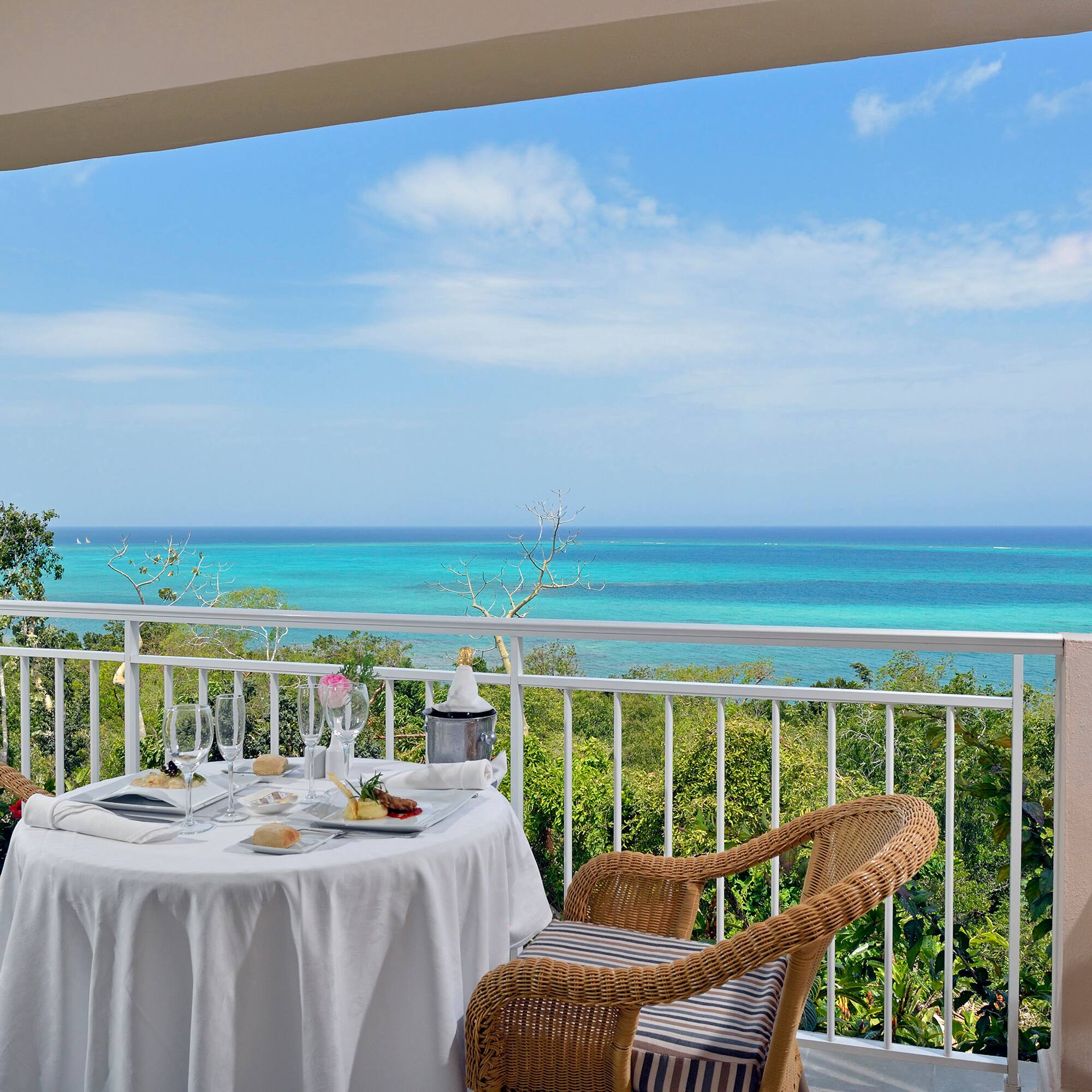 a table with a chair and a table set on a balcony overlooking the ocean