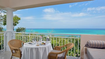 a table with a chair and a table set on a balcony overlooking the ocean