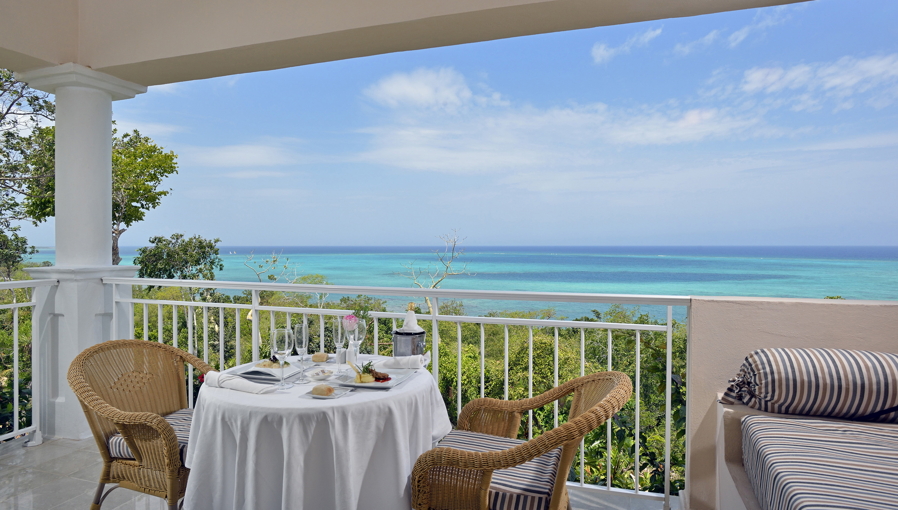 a table with a chair and a table set on a balcony overlooking the ocean