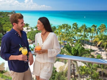 a man and woman holding drinks on a balcony overlooking a beach