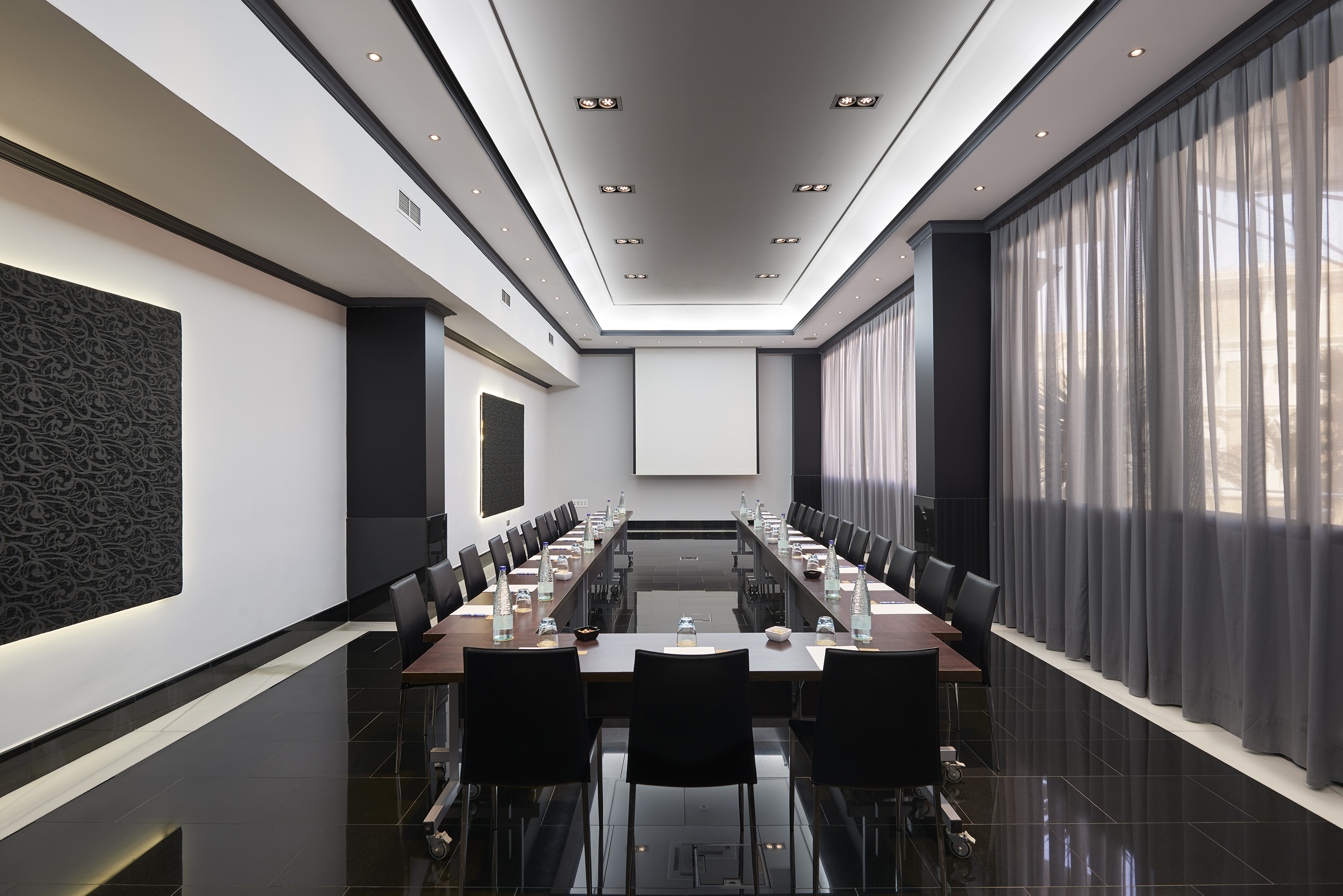 Professional conference room with U-shaped table setup and projector screen.
