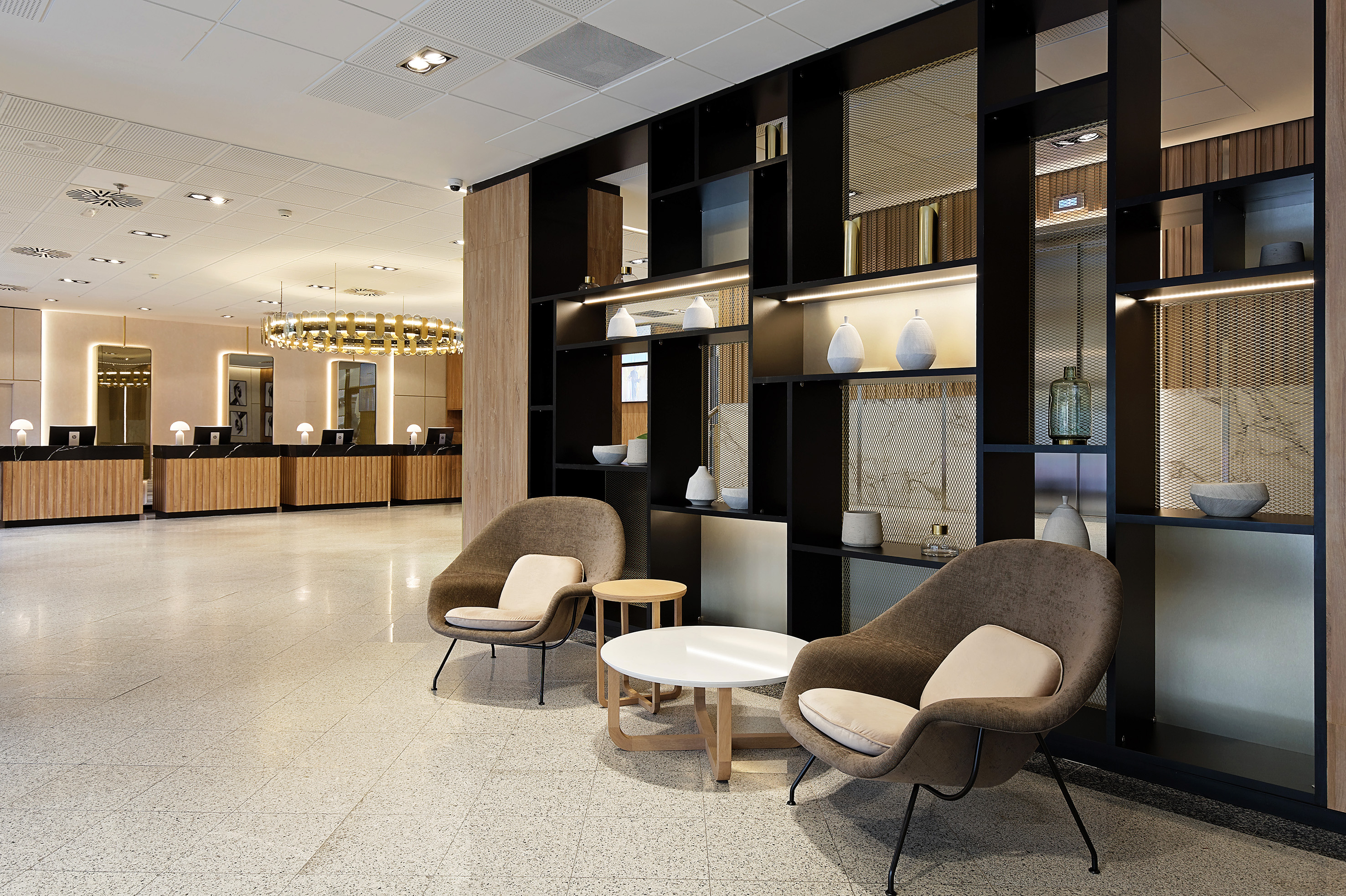 Modern hotel lobby with reception desks, lounge seating, and decorative shelving.