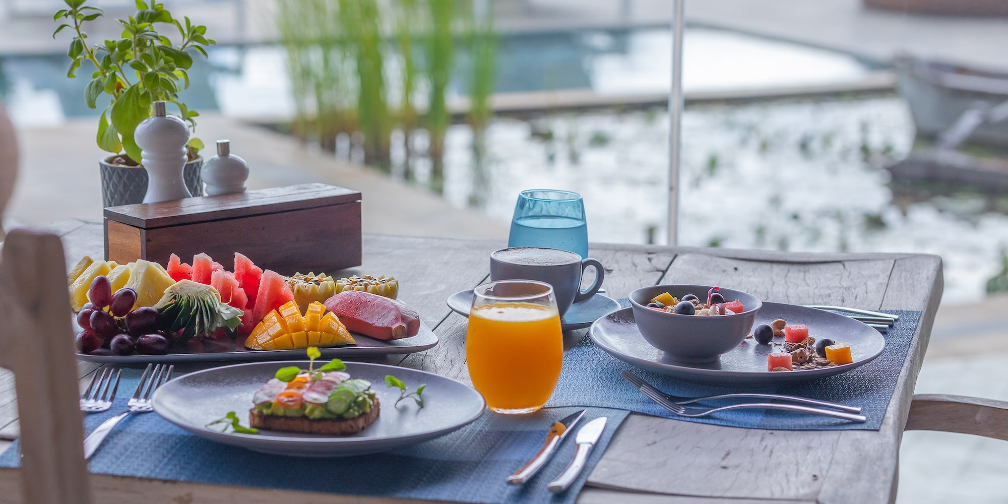 Healthy tropical breakfast: fruit platter, avocado toast, coffee, poolside resort.