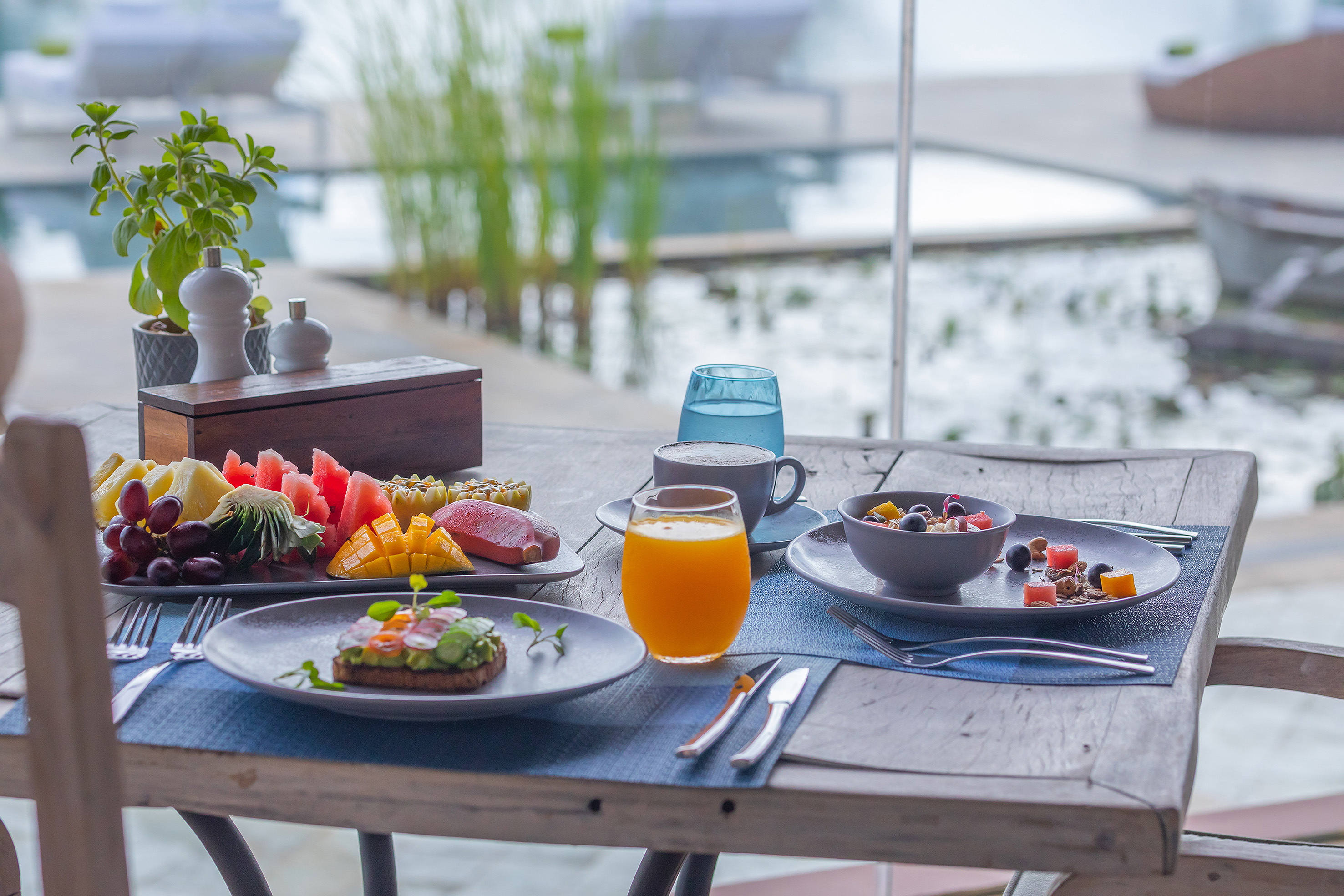 Healthy tropical breakfast: fruit platter, avocado toast, coffee, poolside resort.