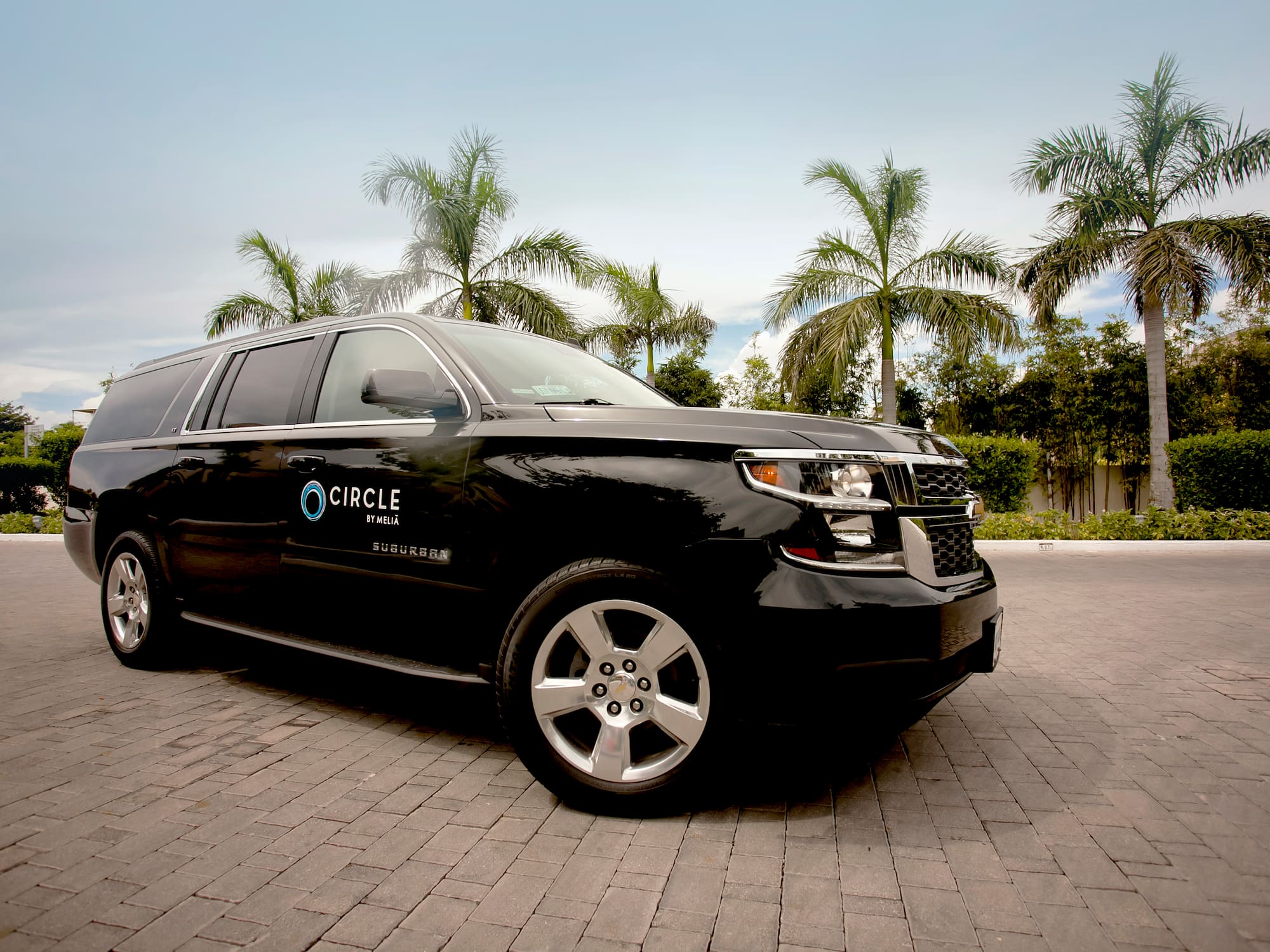 a black suv parked on brick road with palm trees in the background