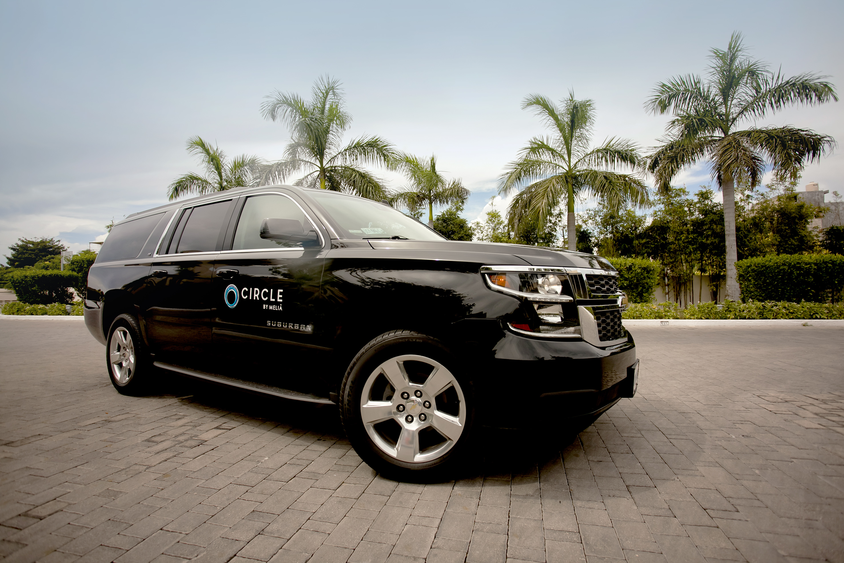 a black suv parked on brick road with palm trees in the background