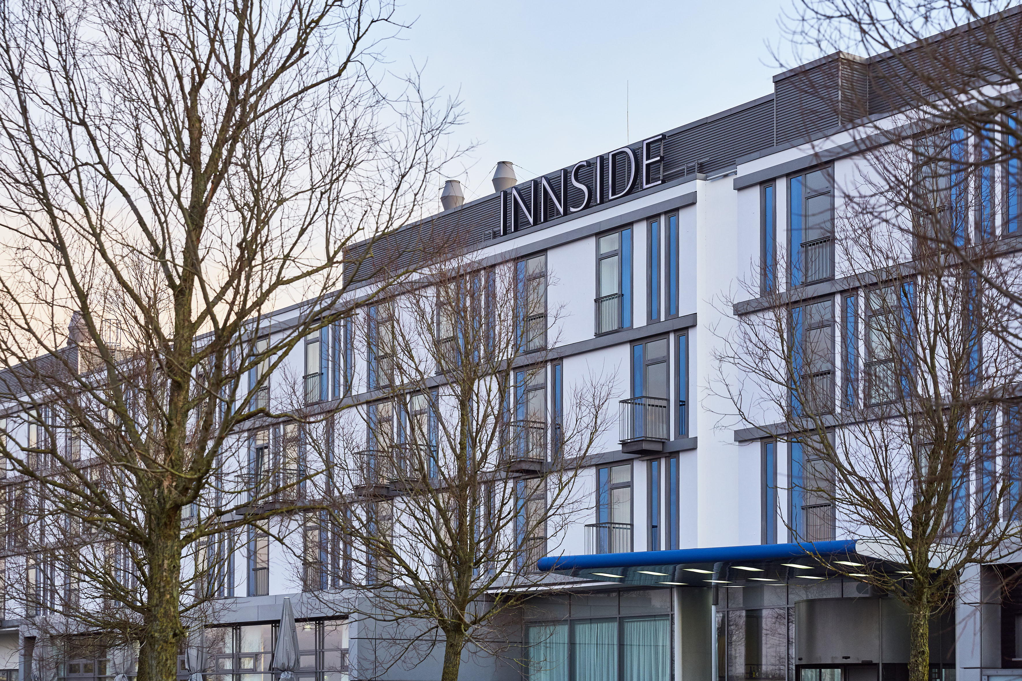 INNSIDE hotel building exterior, modern white and grey facade, bare trees.